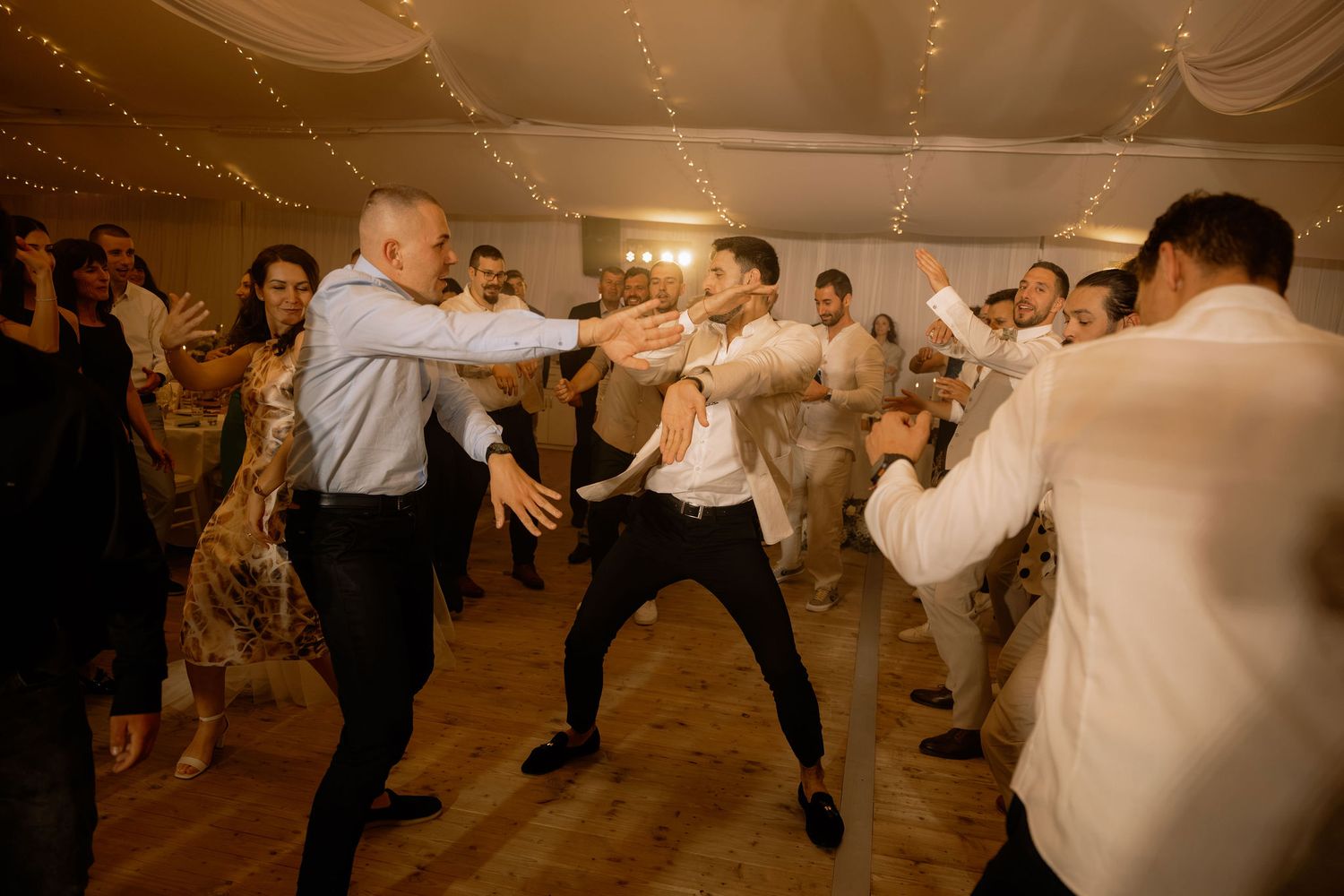 Guests dancing energetically at a wedding reception in a warmly lit venue with fairy lights.
