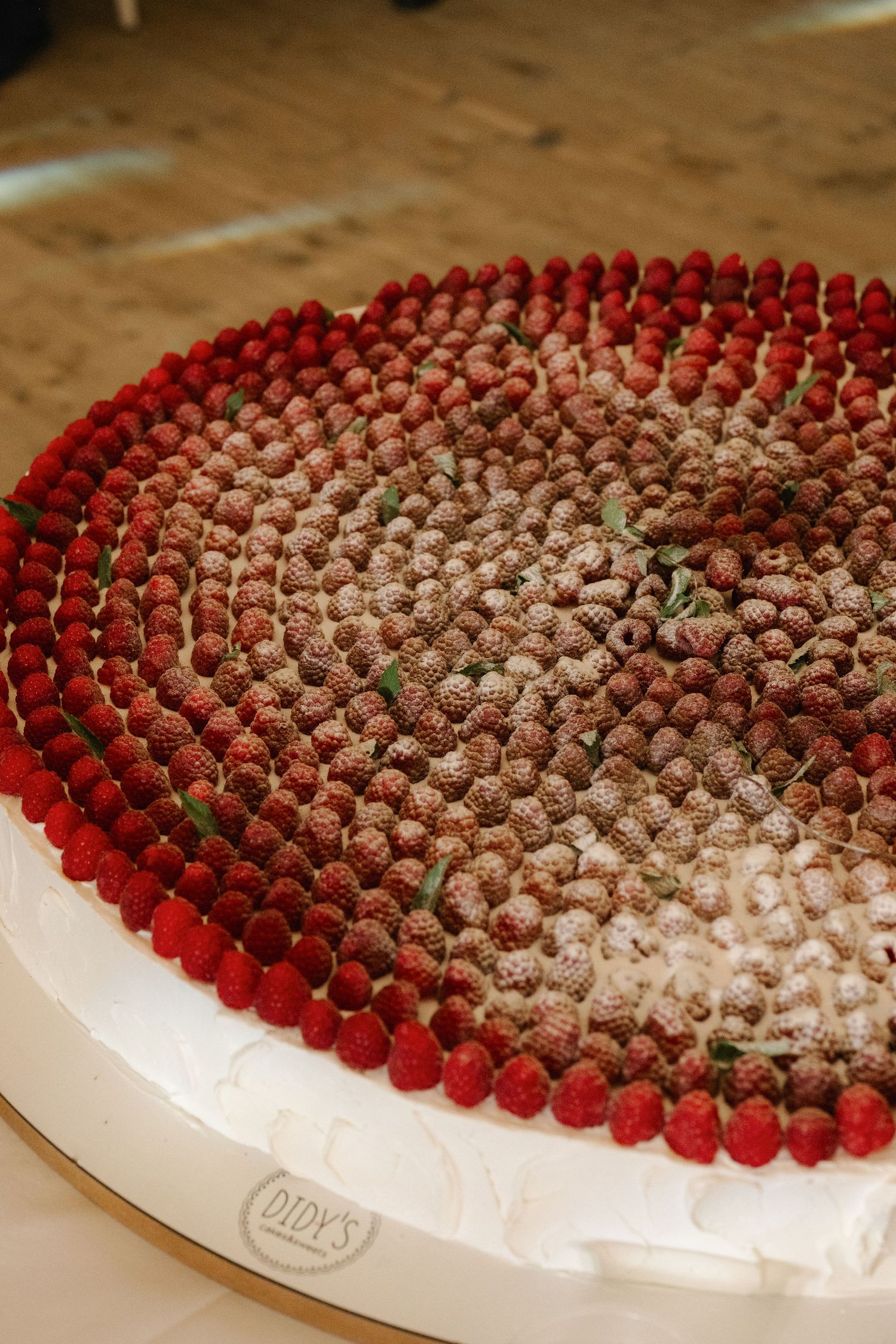 Large round cake topped with rows of fresh raspberries dusted with powdered sugar, from Didy's bakery.