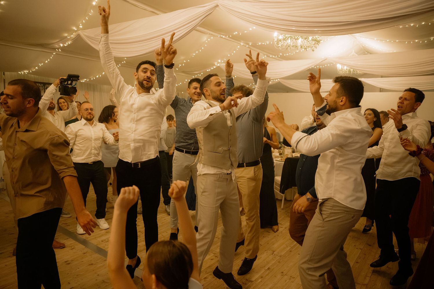 Guests dancing joyfully at a wedding reception under fairy lights in a decorated venue.