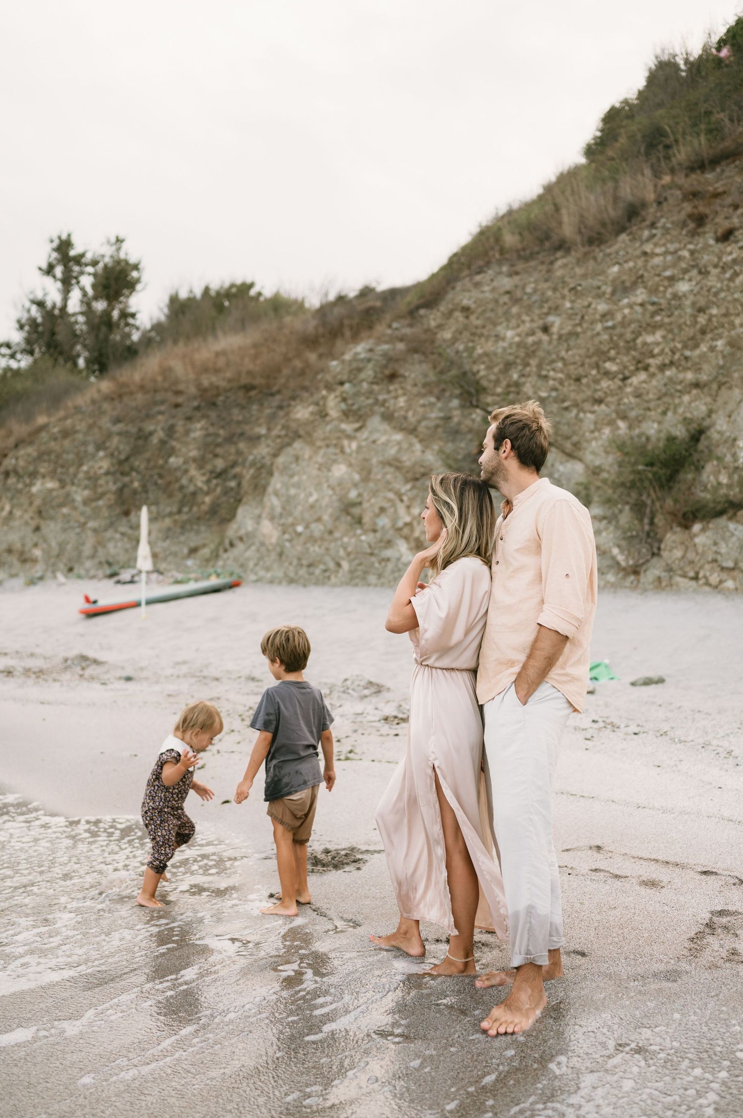 Family of four enjoying a peaceful barefoot walk on a sandy beach with rocky cliffs in the background.