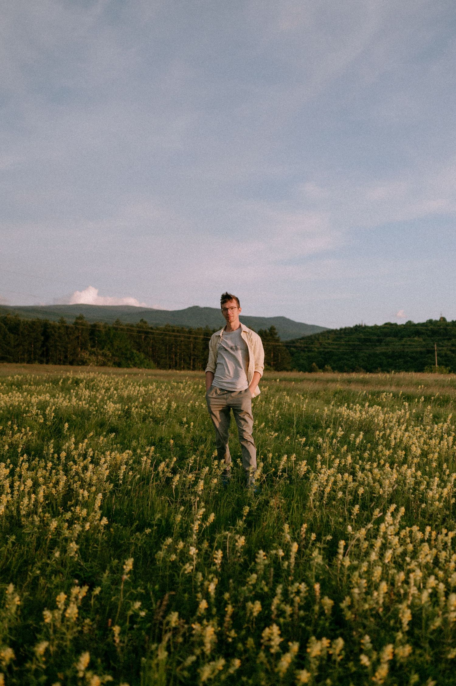 Person standing in a vast field of yellow flowers against mountain backdrop.