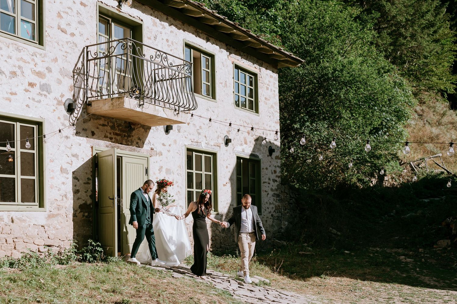 Guests mingle on the grounds of a charming stone villa surrounded by lush greenery.