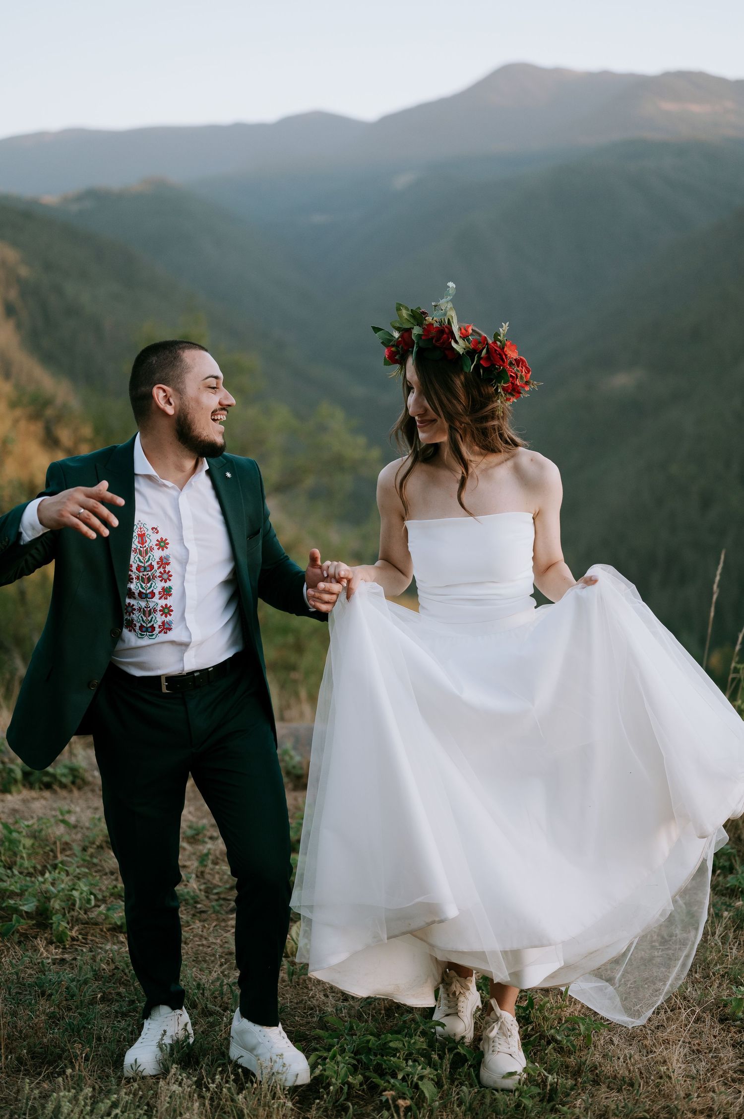 Bride and groom in casual wedding attire dance together on a mountain overlook.