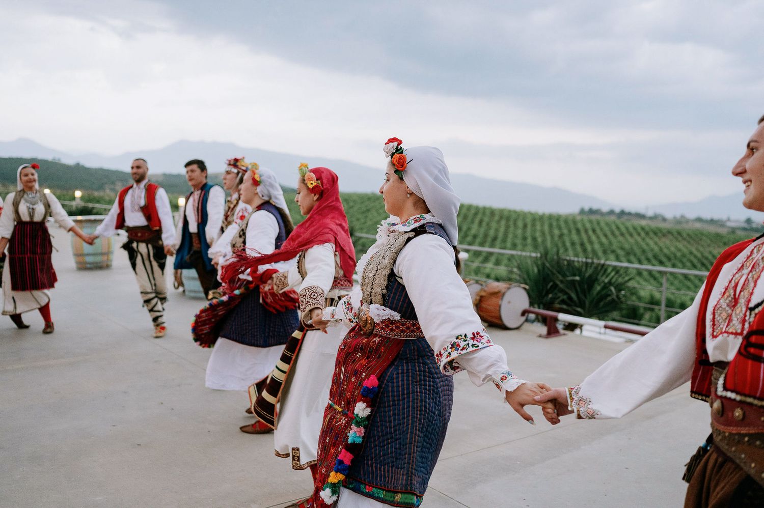 Traditional dancers in folk costumes perform on an outdoor terrace with vineyard views.