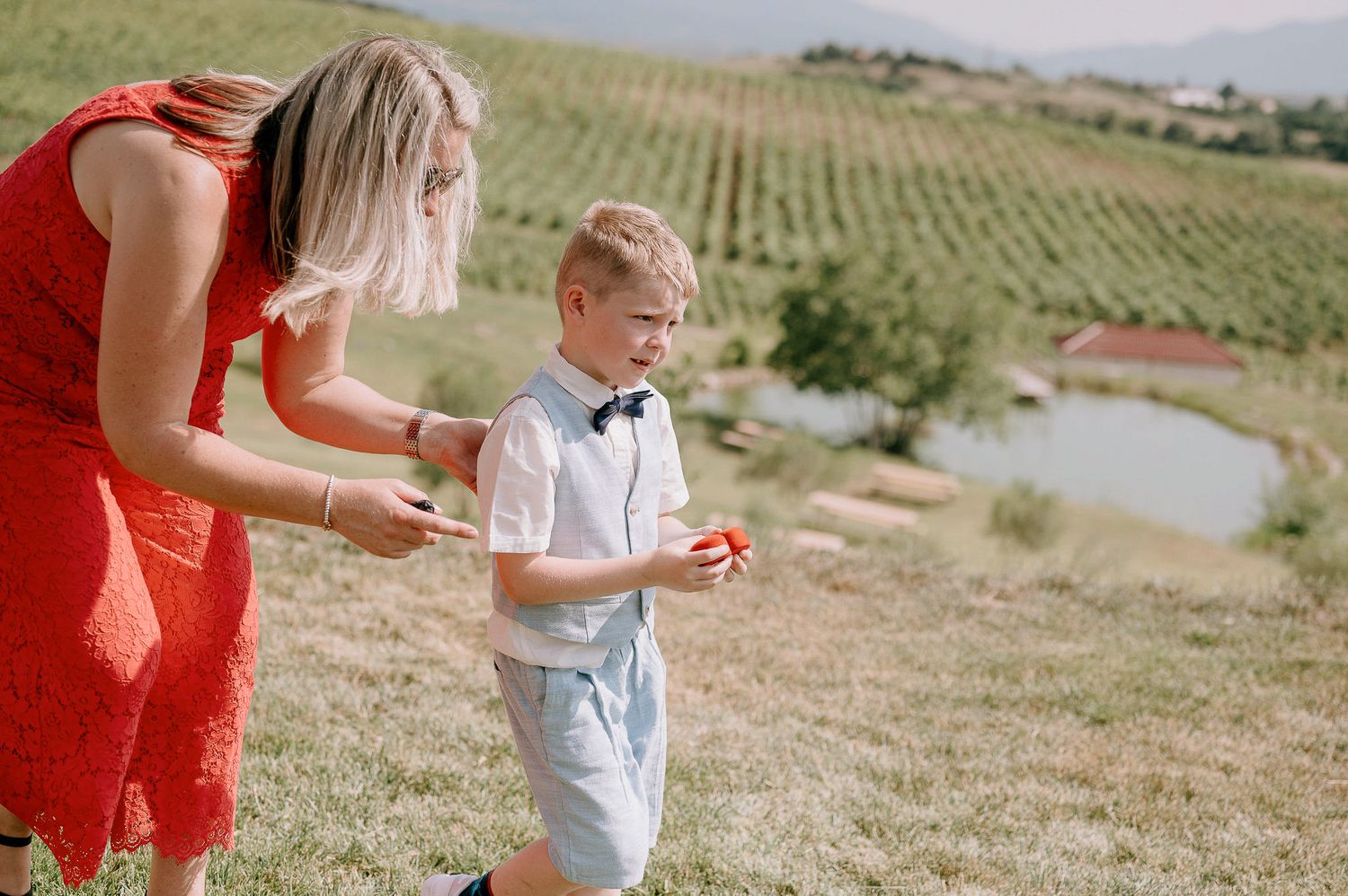 Wedding celebration on sunny hillside with guests in red and white attire.