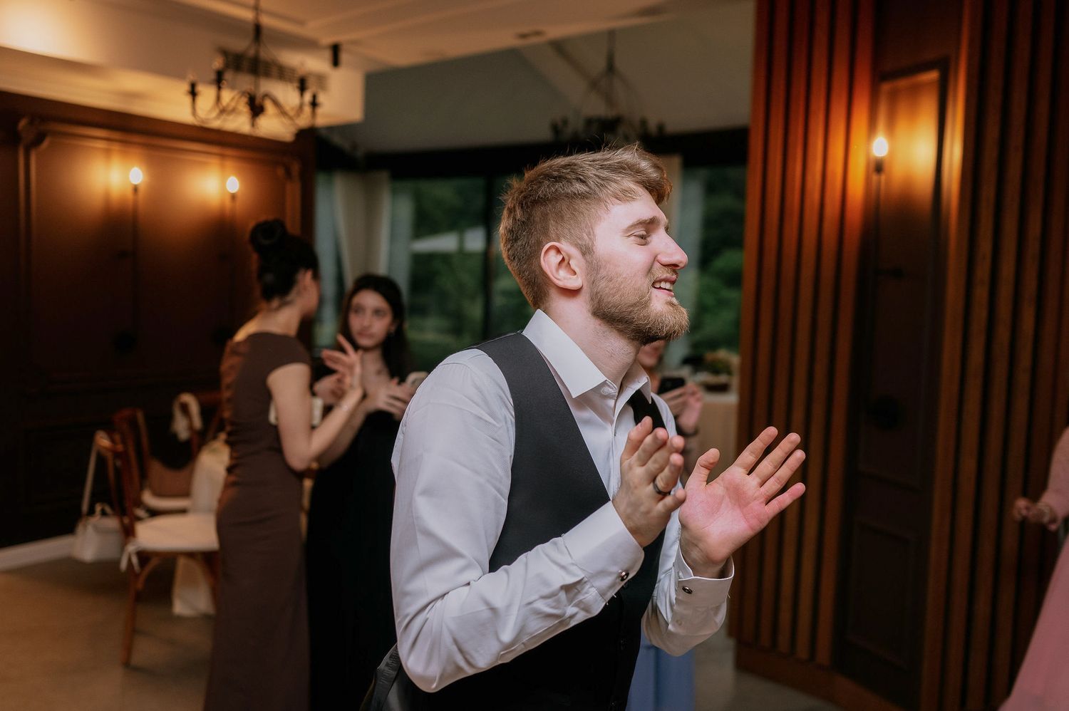 Wedding reception guests dancing and celebrating in a dimly lit venue with warm lighting.