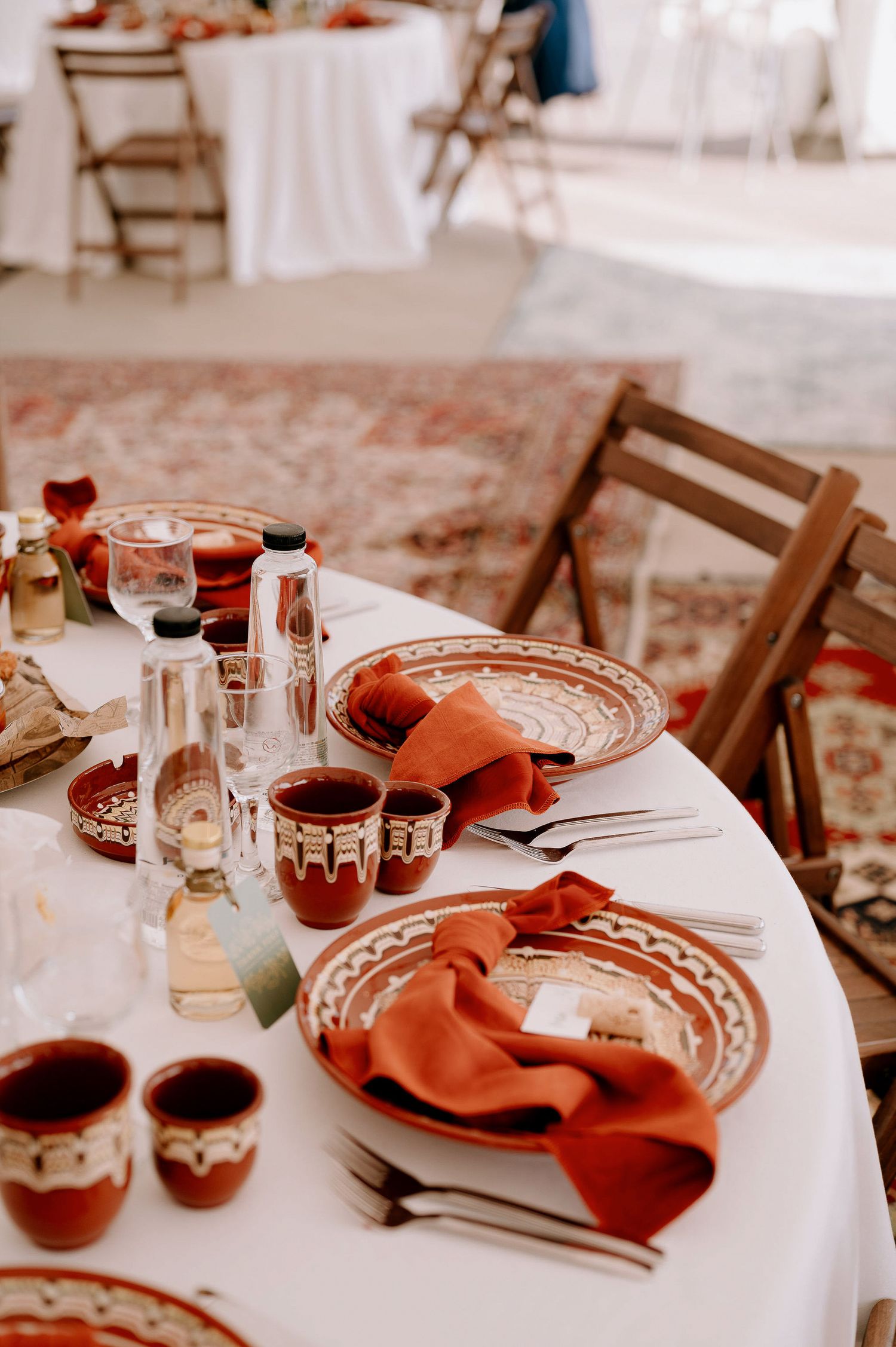 Elegant table setting with terracotta napkins and patterned plates on white tablecloth.