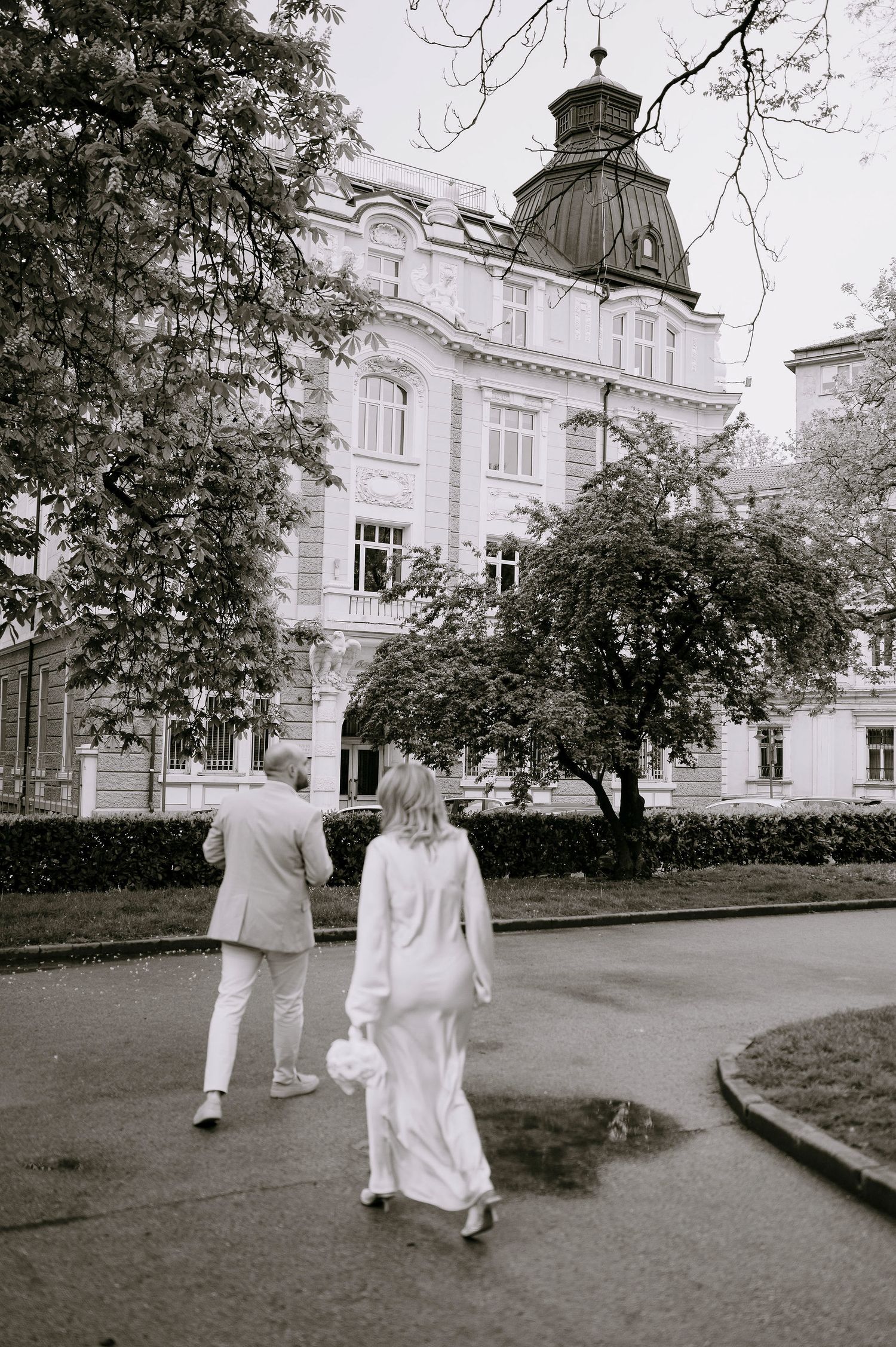 Two people in white attire walk along a path outside a grand historic building.