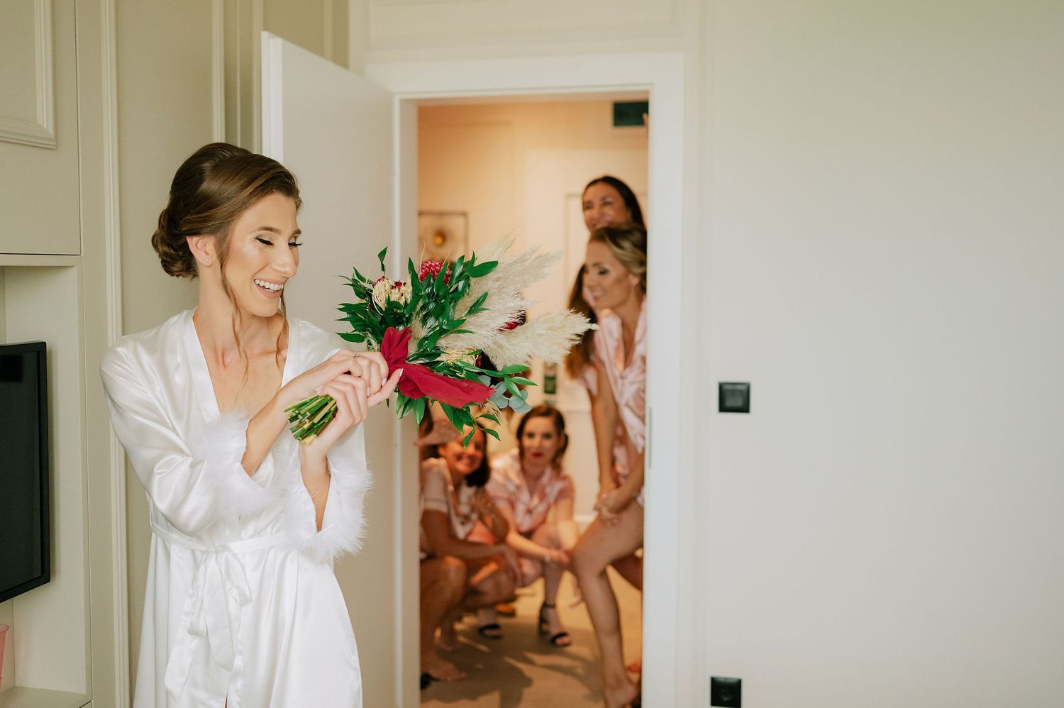 Wedding preparations in a bright interior room with white robes and joyful atmosphere.