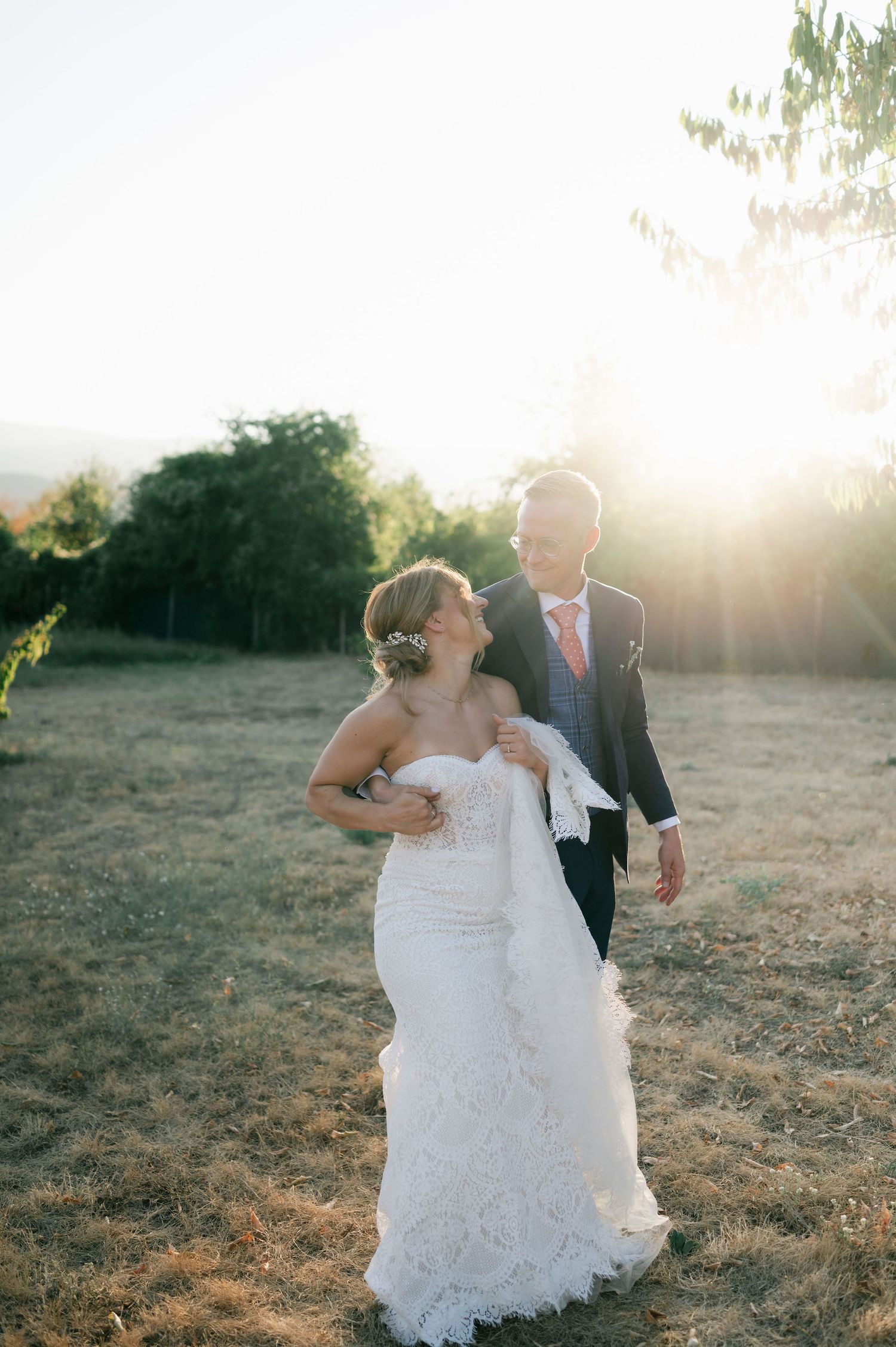 Newlyweds share a romantic dance in a sun-drenched field during golden hour.