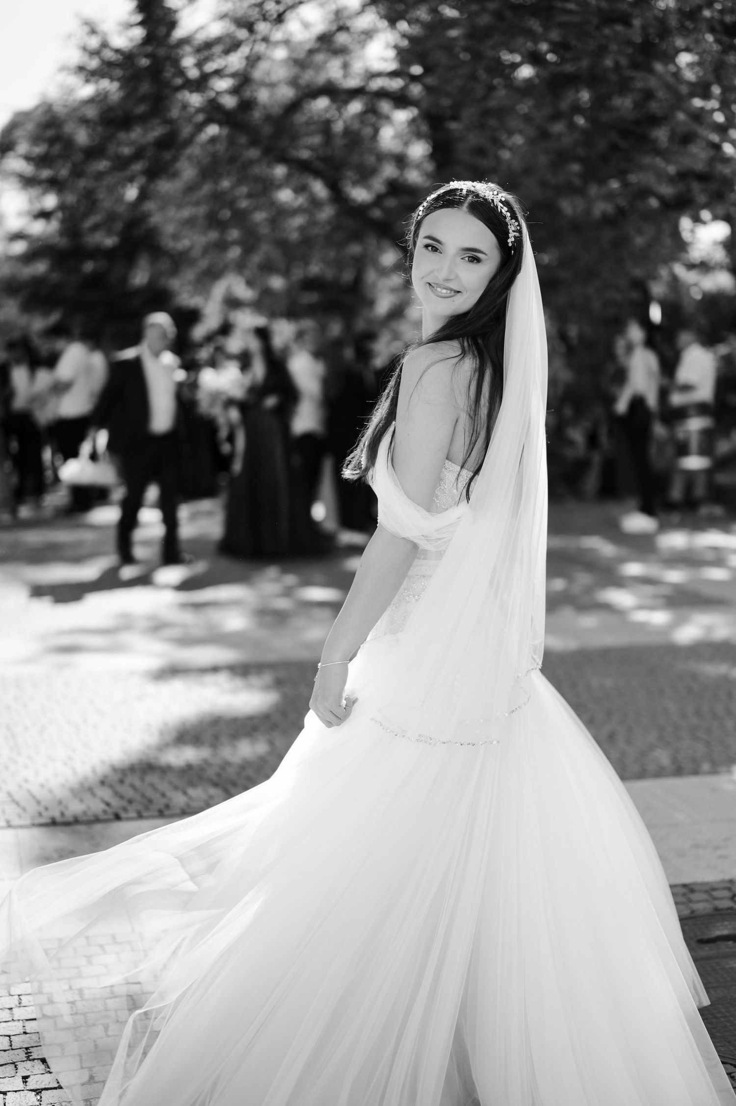 Bride twirls in flowing white wedding gown outdoors in a garden setting.