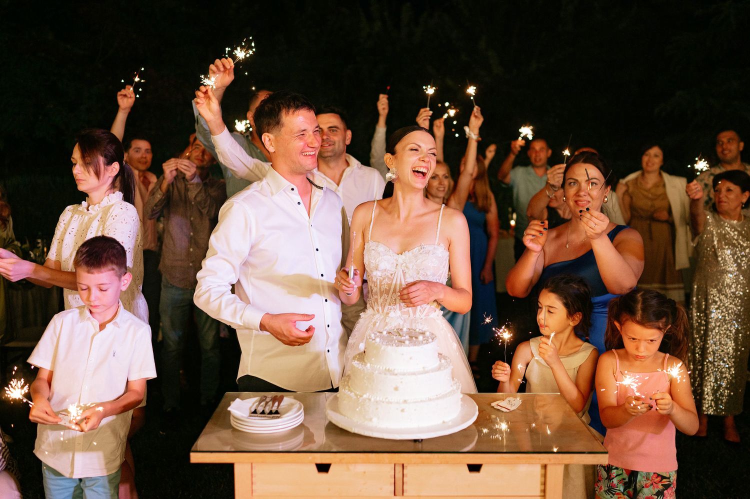 Wedding guests celebrate with the couple during a lively reception under string lights.