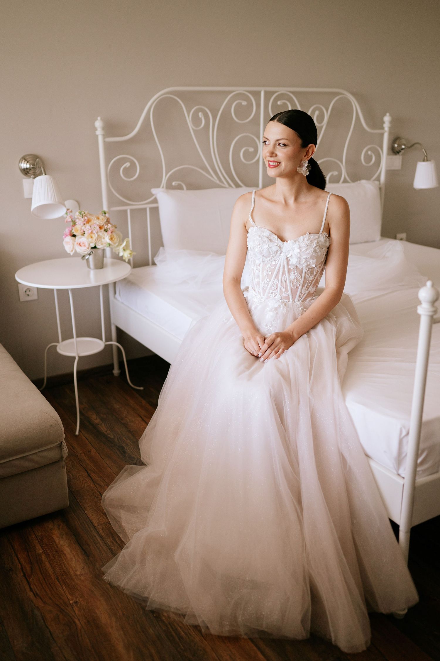 Dreamy bridal portrait showing intricate details of white wedding dress against ornate bed frame.