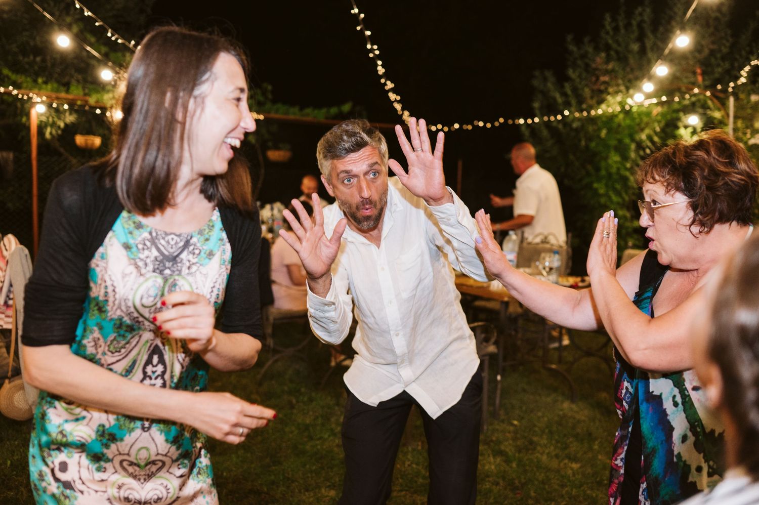 Wedding guests dance and celebrate under string lights at outdoor evening reception.