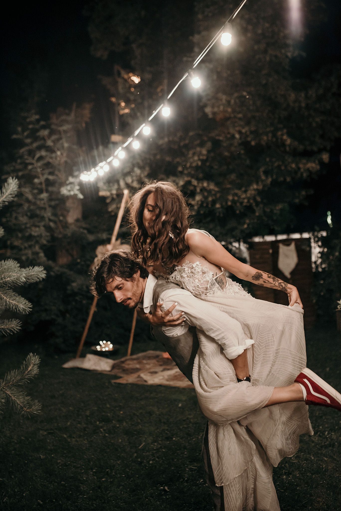 A romantic couple dances and embraces under glowing string lights at an evening outdoor wedding reception.