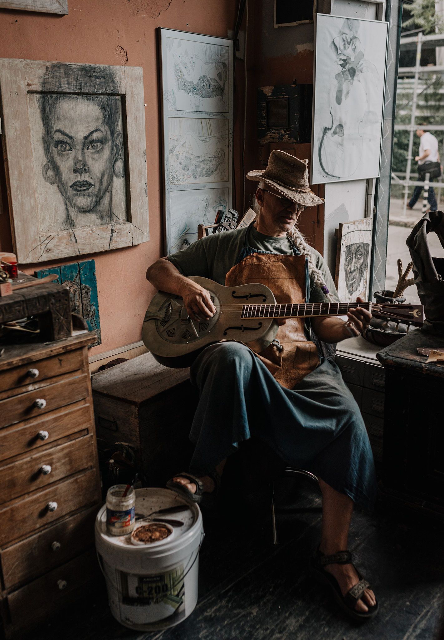 Artist's studio with sketches on walls and someone playing guitar in dim lighting.