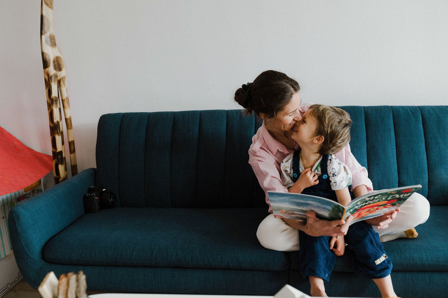 Parent and child sit together on a teal couch while reading a book and sharing quality time.