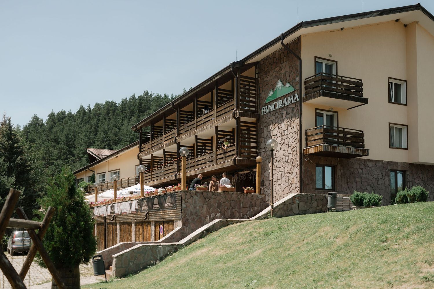 Rustic mountain lodges with wooden balconies nestled on a green hillside surrounded by pine forest.