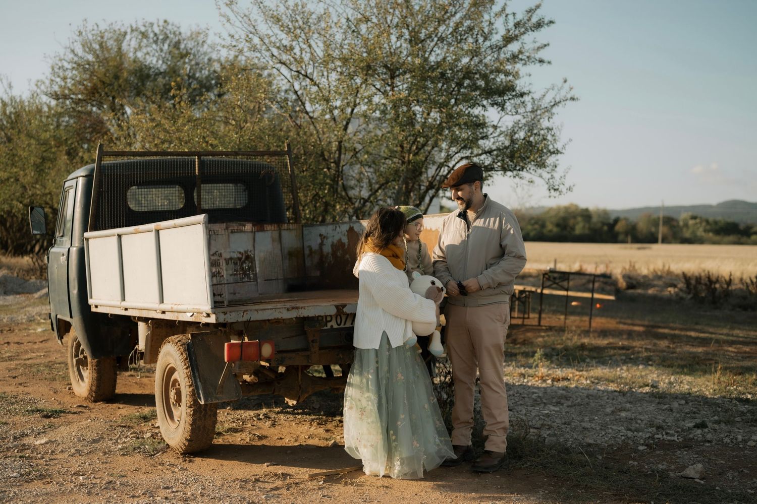 A vintage truck sits in a desert landscape with people gathered around it during a rustic outdoor wedding ceremony.