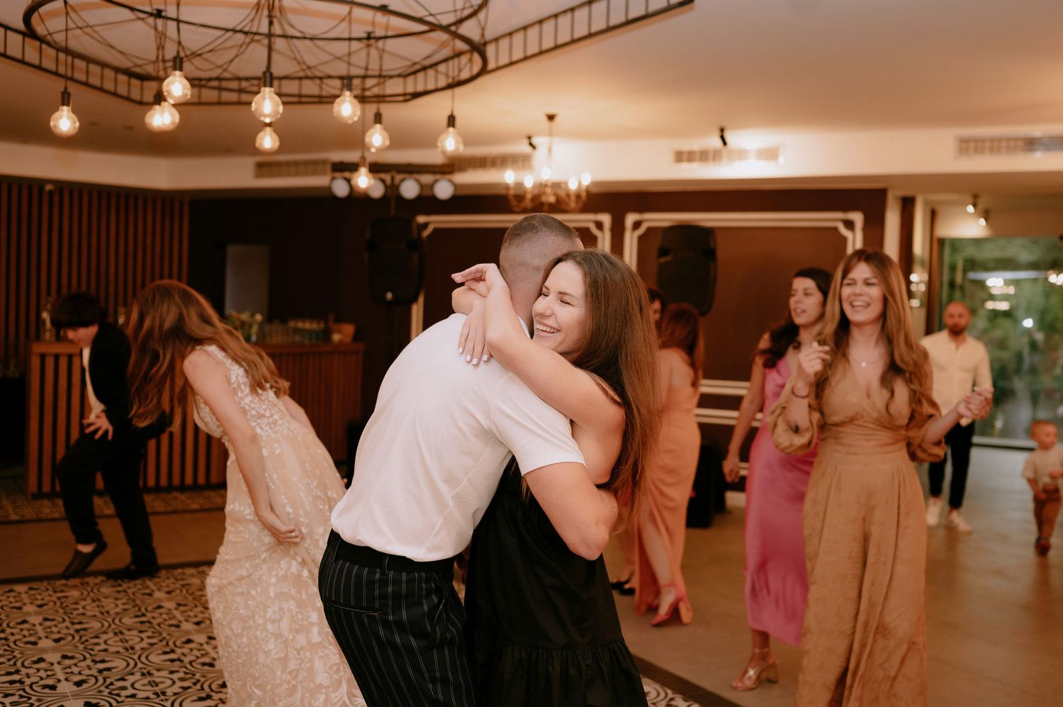 Couples dance across an elegant ballroom floor illuminated by warm lighting during a wedding celebration.