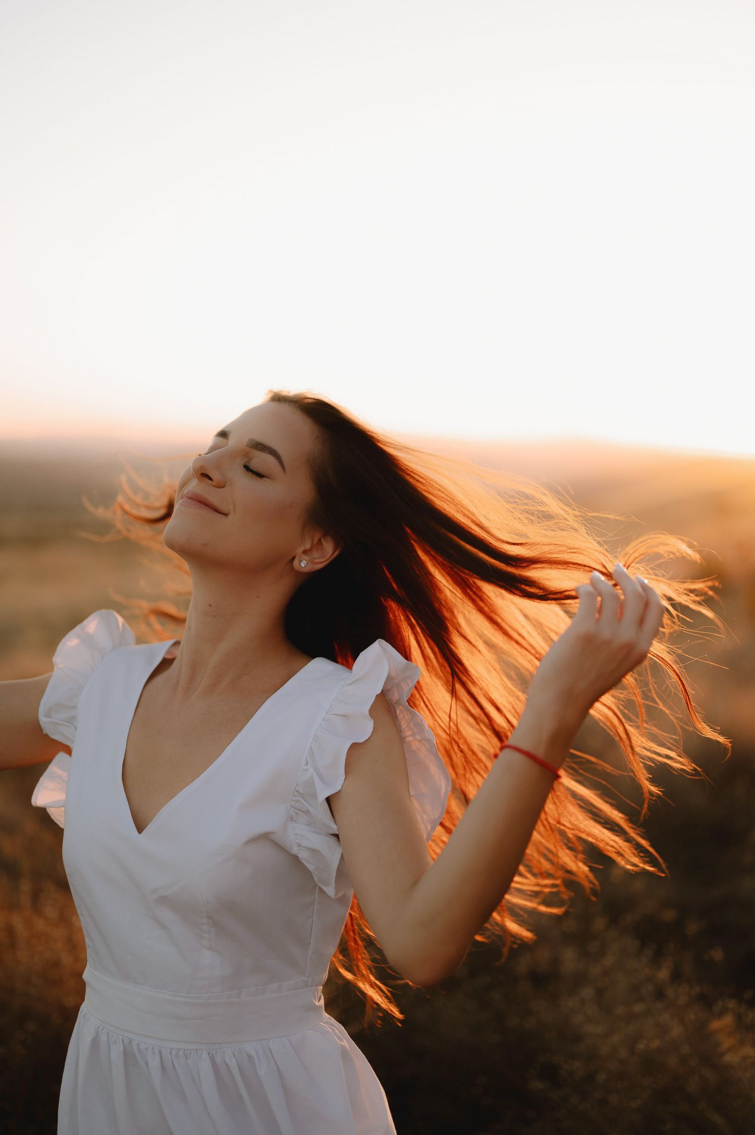 A person in a white dress twirls with flowing hair against a warm sunset backdrop creating a dreamy atmosphere.