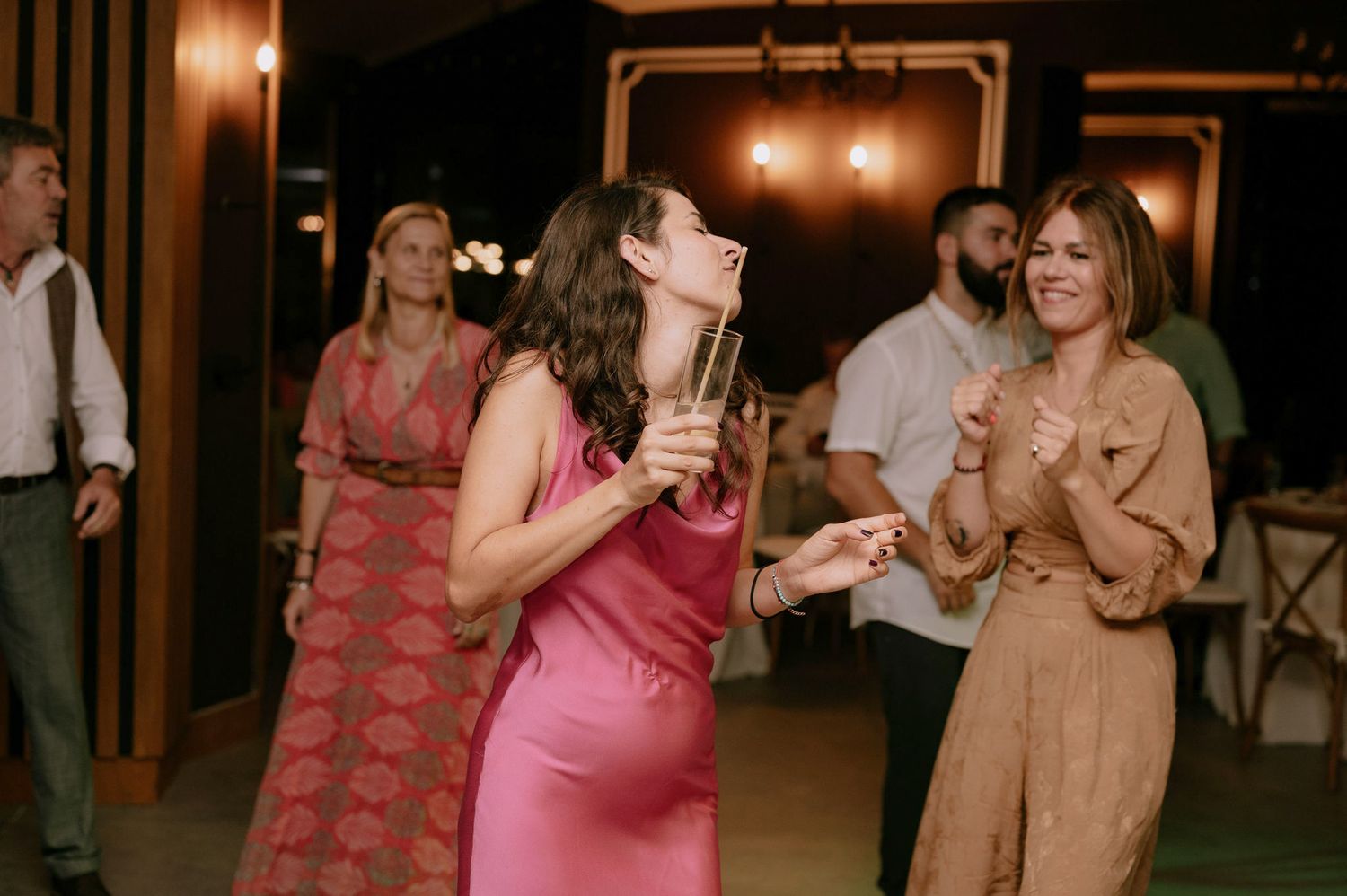 People dancing and enjoying themselves at a dimly lit party venue with warm lighting and festive atmosphere.