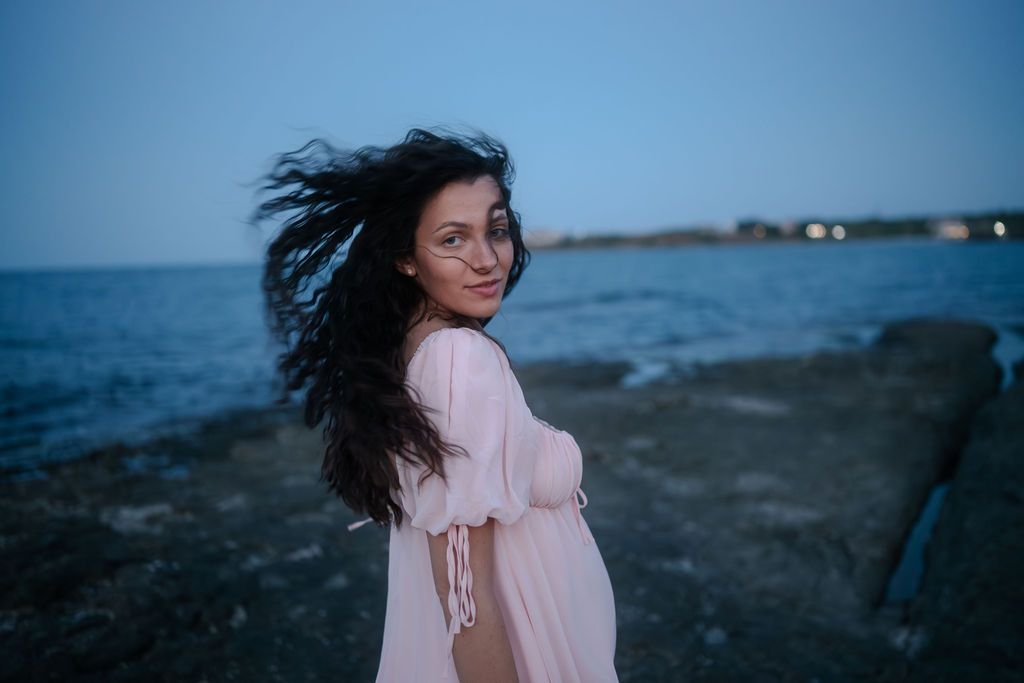 A person in a pink dress walks along a scenic beach shoreline at dusk.