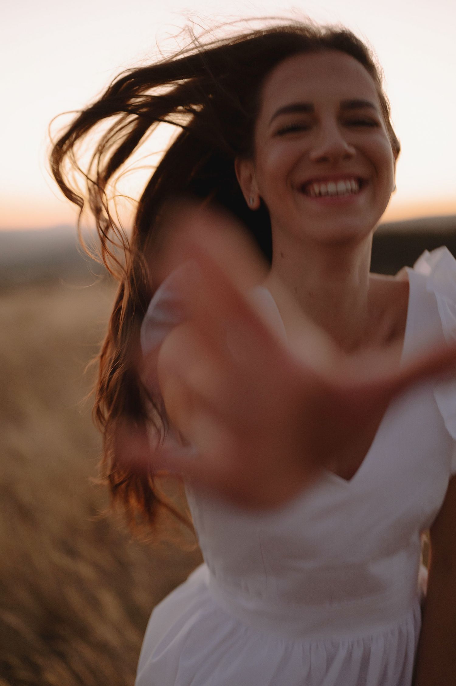 A joyful person in a white dress spins and dances in a golden field at sunset.