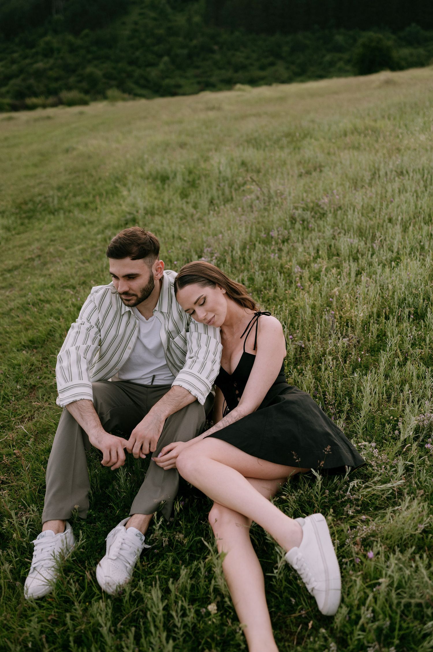 Two people relax together in tall grass on a hillside during golden hour.