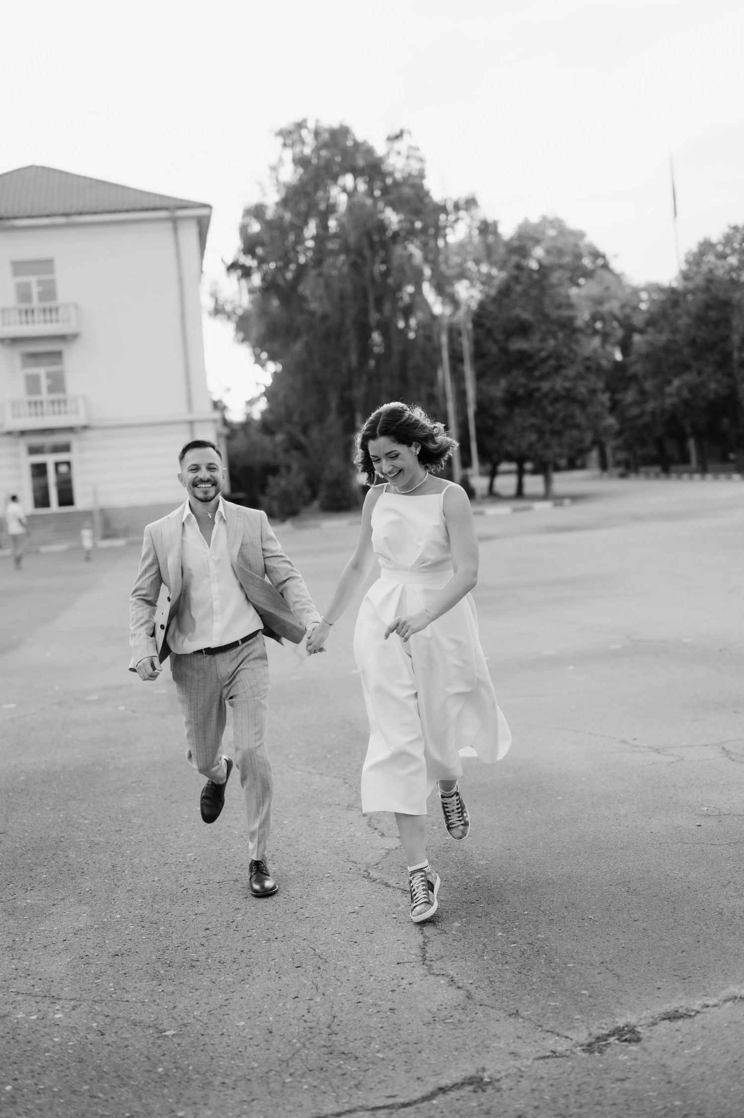 A couple runs playfully across an open field in black and white photography.