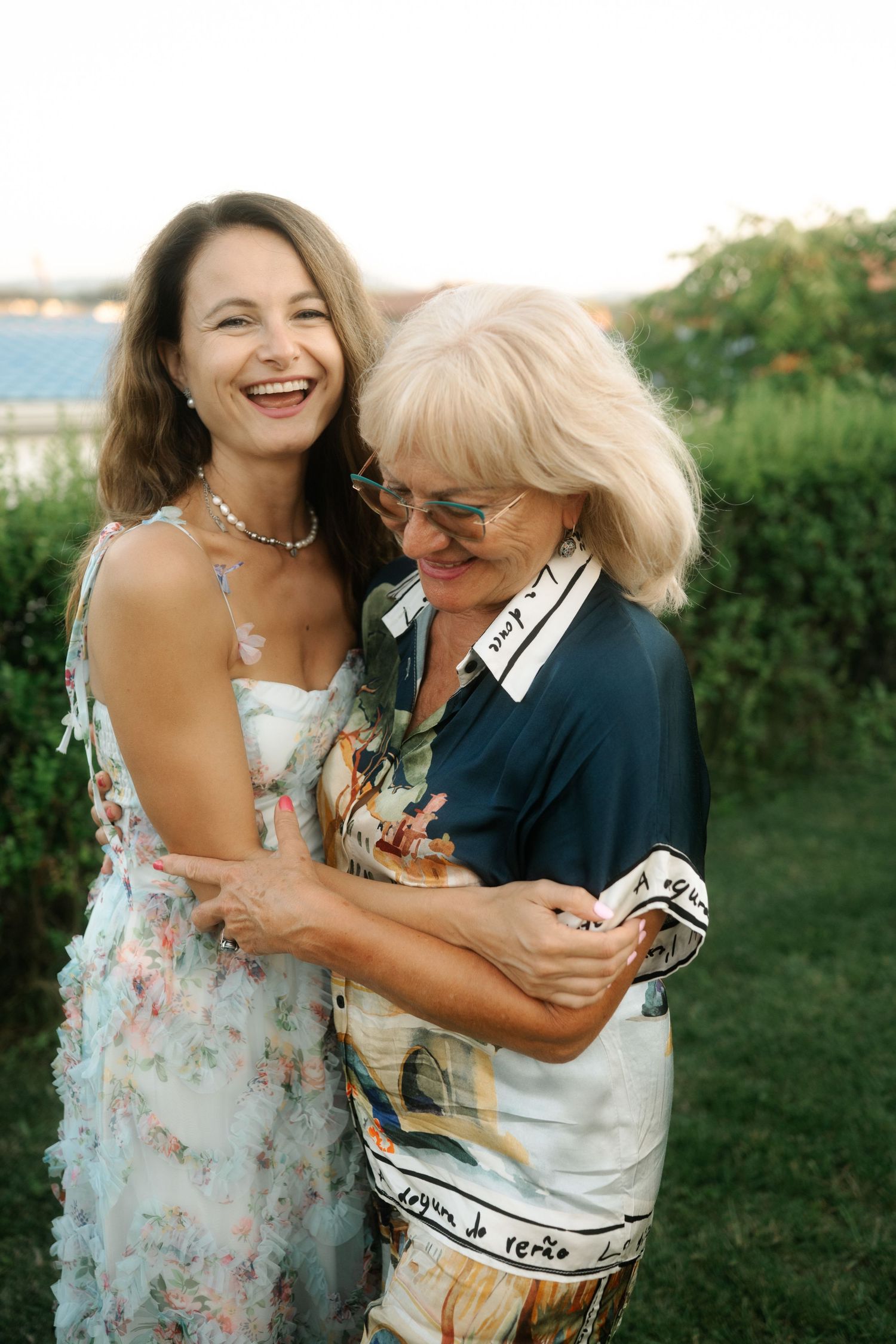 Two people embrace and share joyful laughter together outdoors during a sunny afternoon in a garden setting.