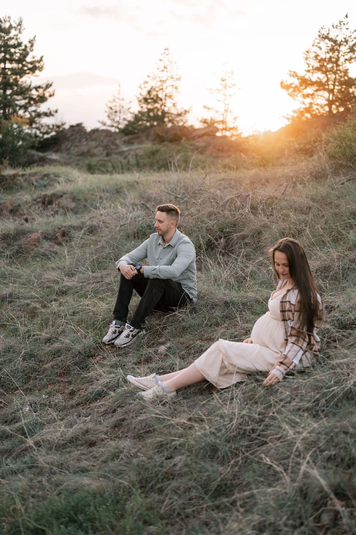 A couple relaxes on a grassy hillside during golden hour sunset, creating a romantic outdoor atmosphere.