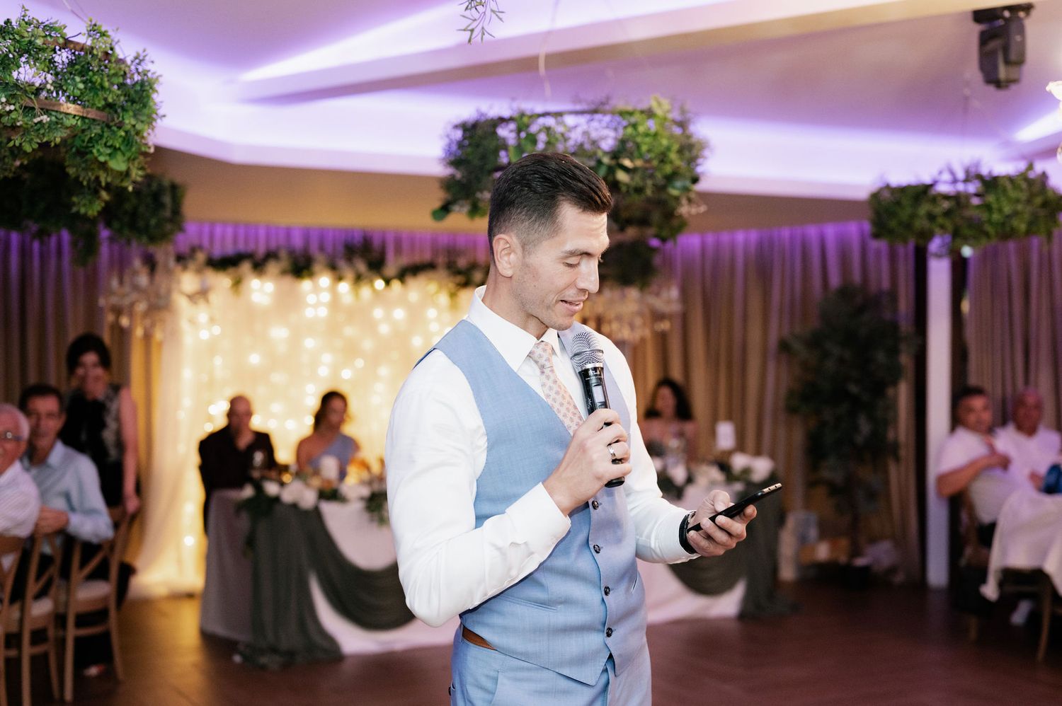People dancing together at a wedding reception under purple mood lighting in an elegant ballroom setting.