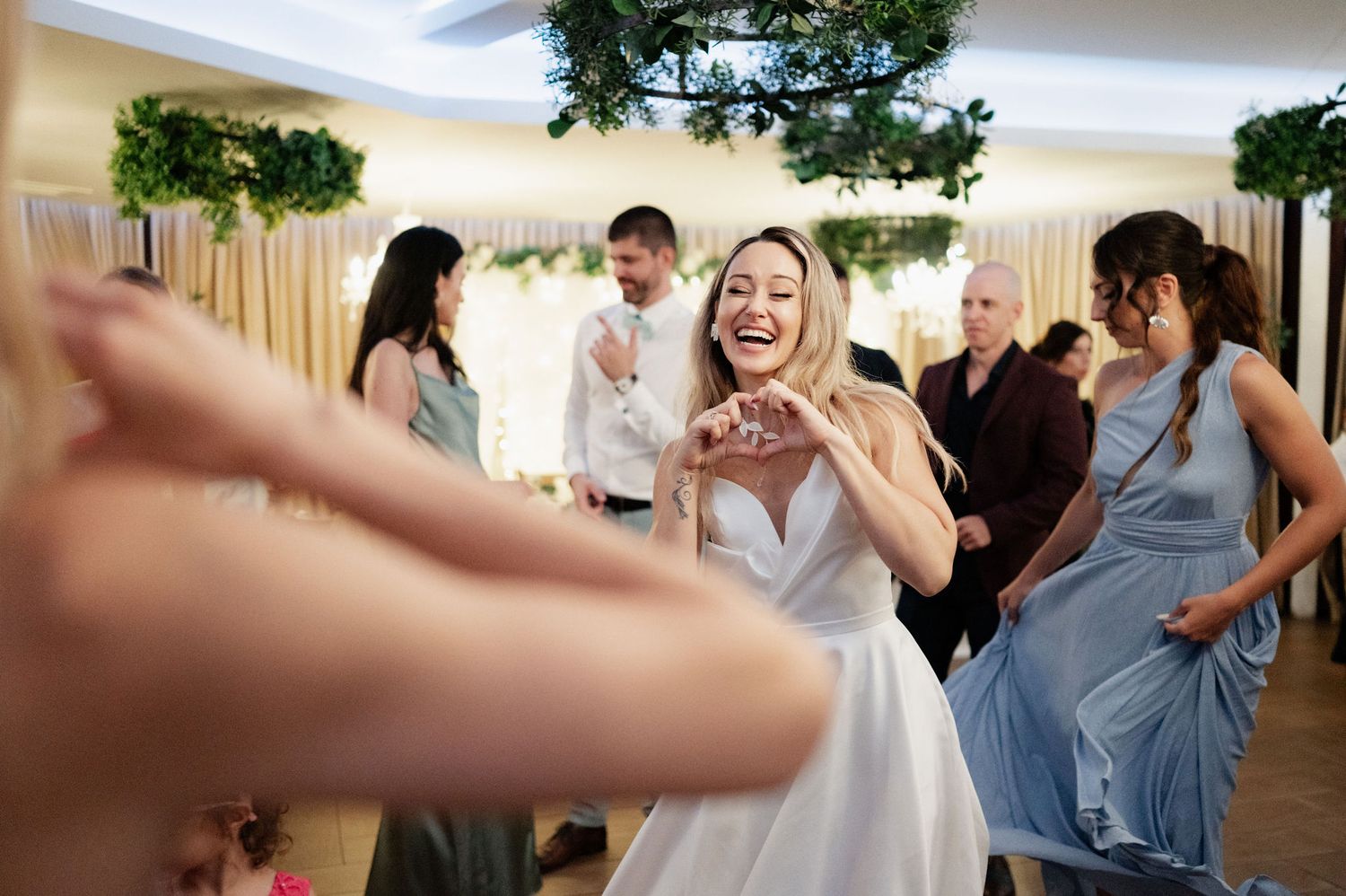 Joyful celebration at a wedding reception as guests dance and laugh together in a decorated indoor venue.