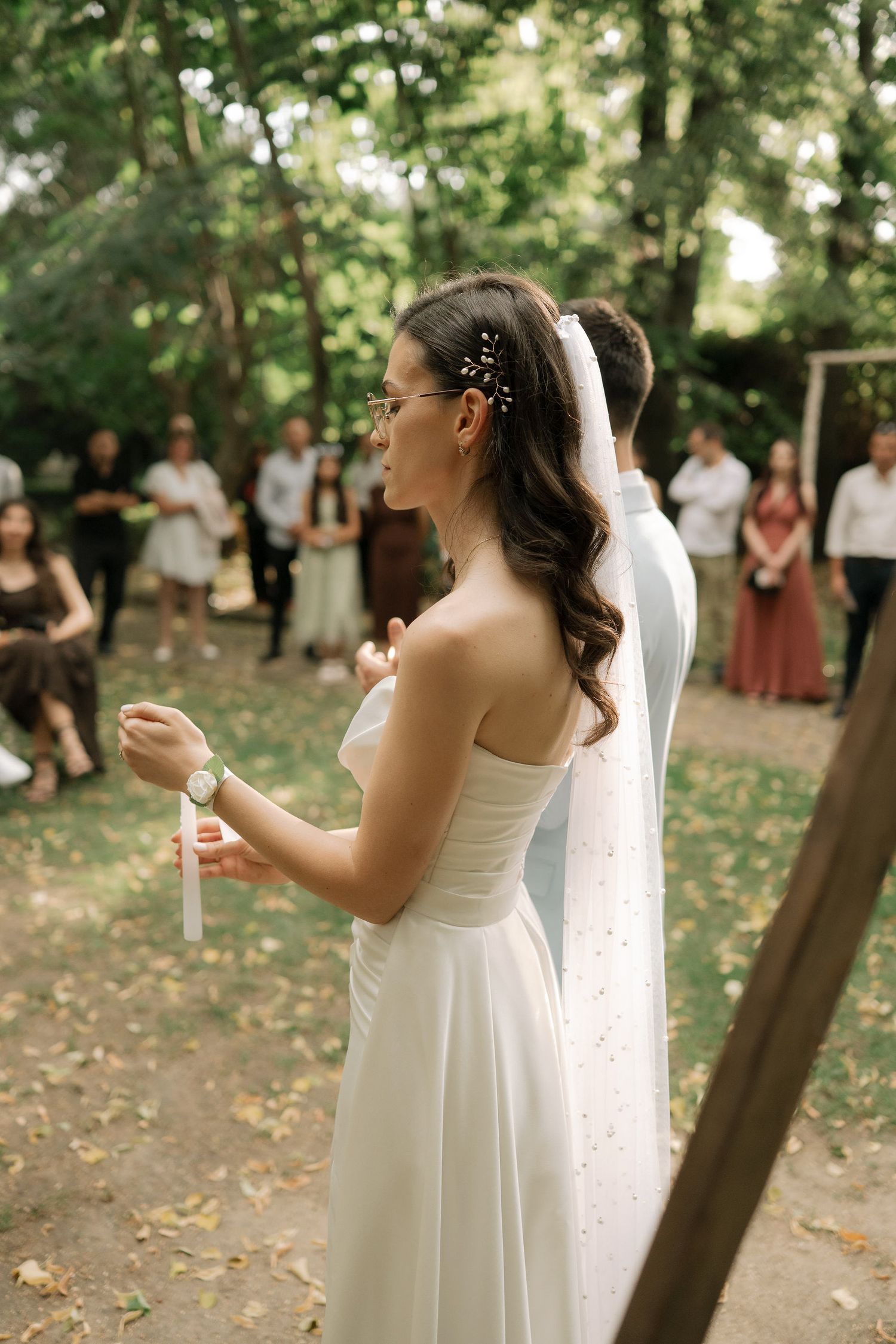 A bride in a white wedding dress blows bubbles during an outdoor woodland ceremony.