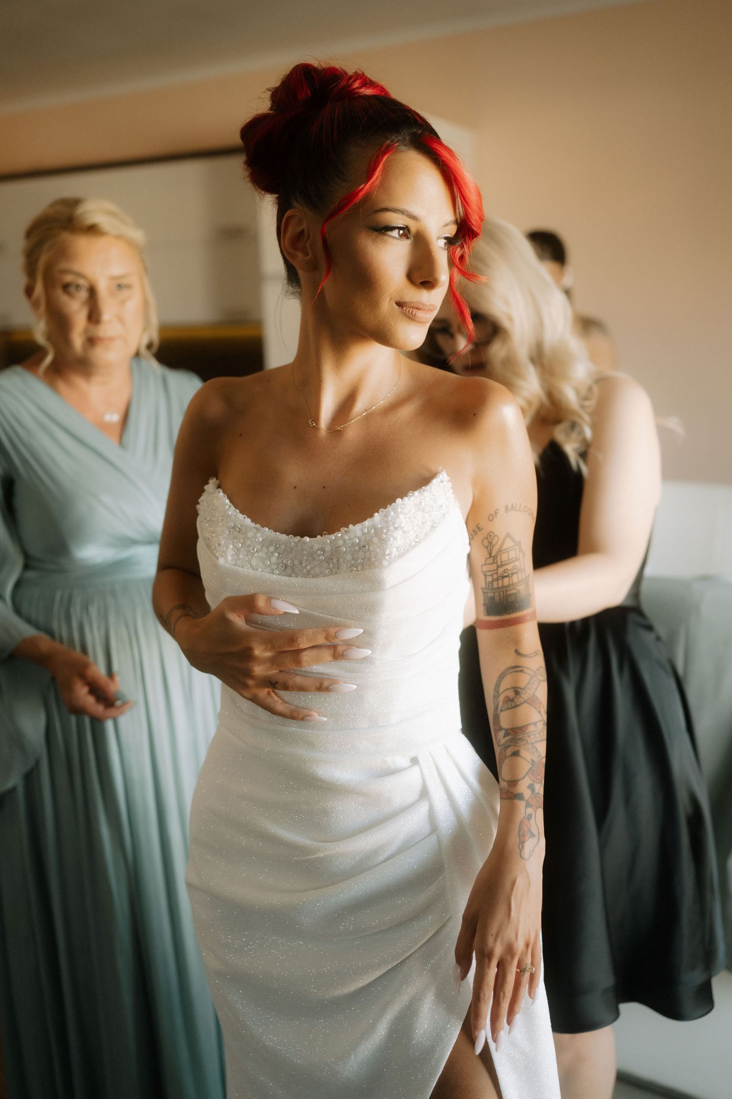 A bride in a white wedding dress shows off her tattoos while bridesmaids in blue dresses look on in the background.