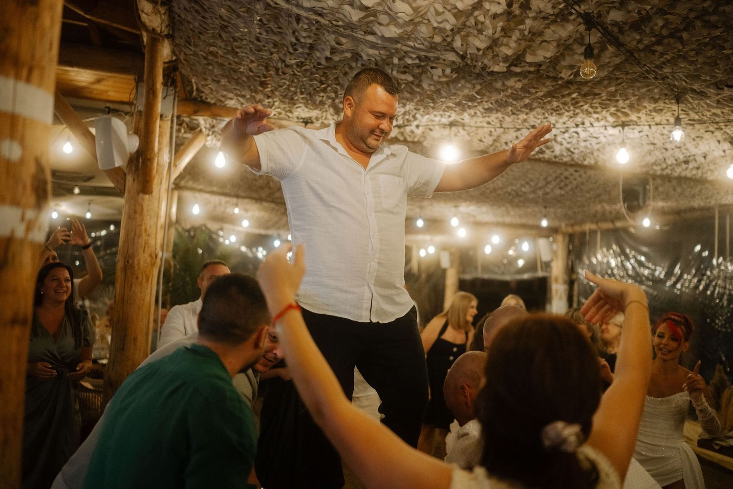 A lively dance party in a rustic underground venue with string lights and exposed stone walls.