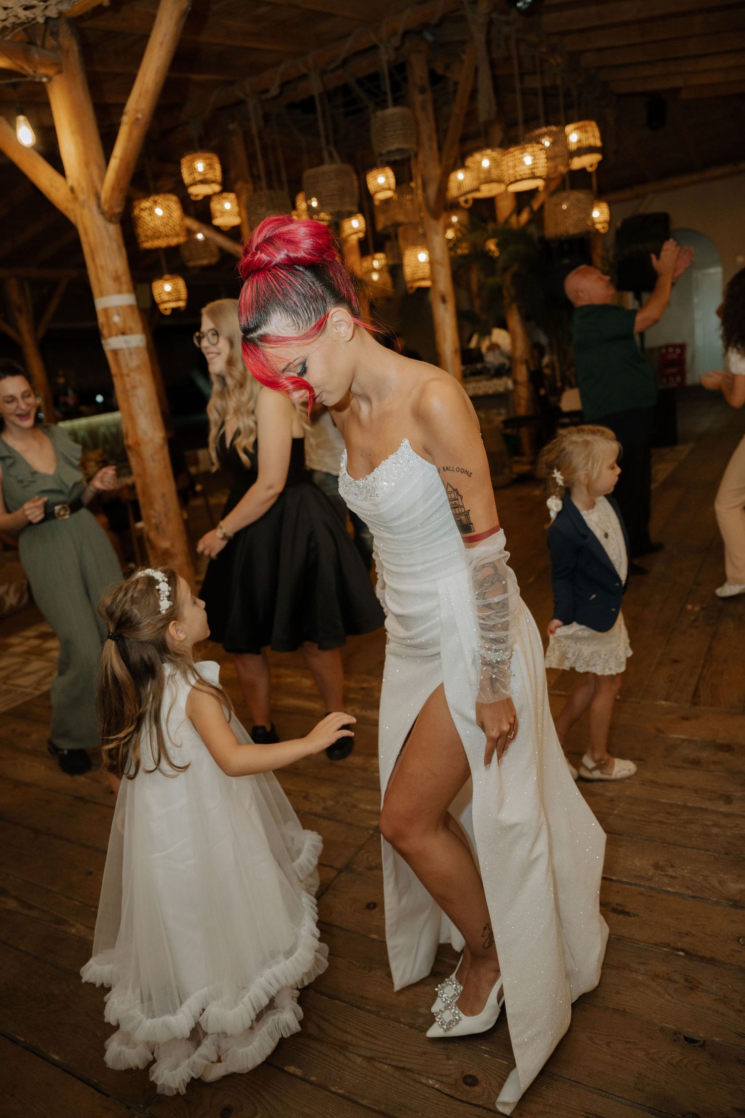 Two people in white outfits dance together at a rustic barn wedding reception with wooden beams and warm lighting.