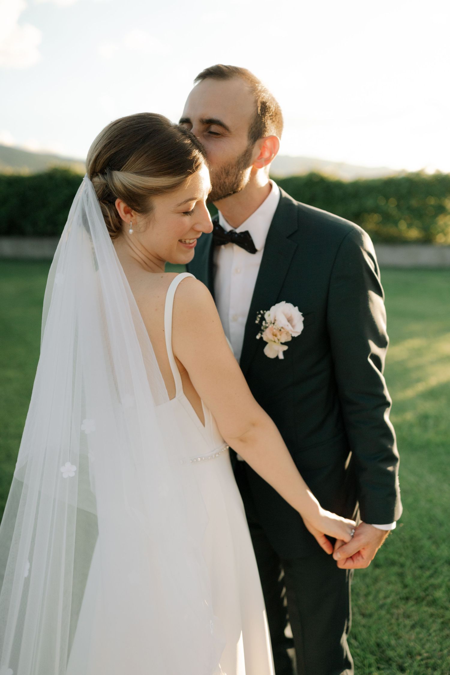 Newlywed couple shares intimate moments in an outdoor wedding photoshoot against a natural landscape at golden hour.