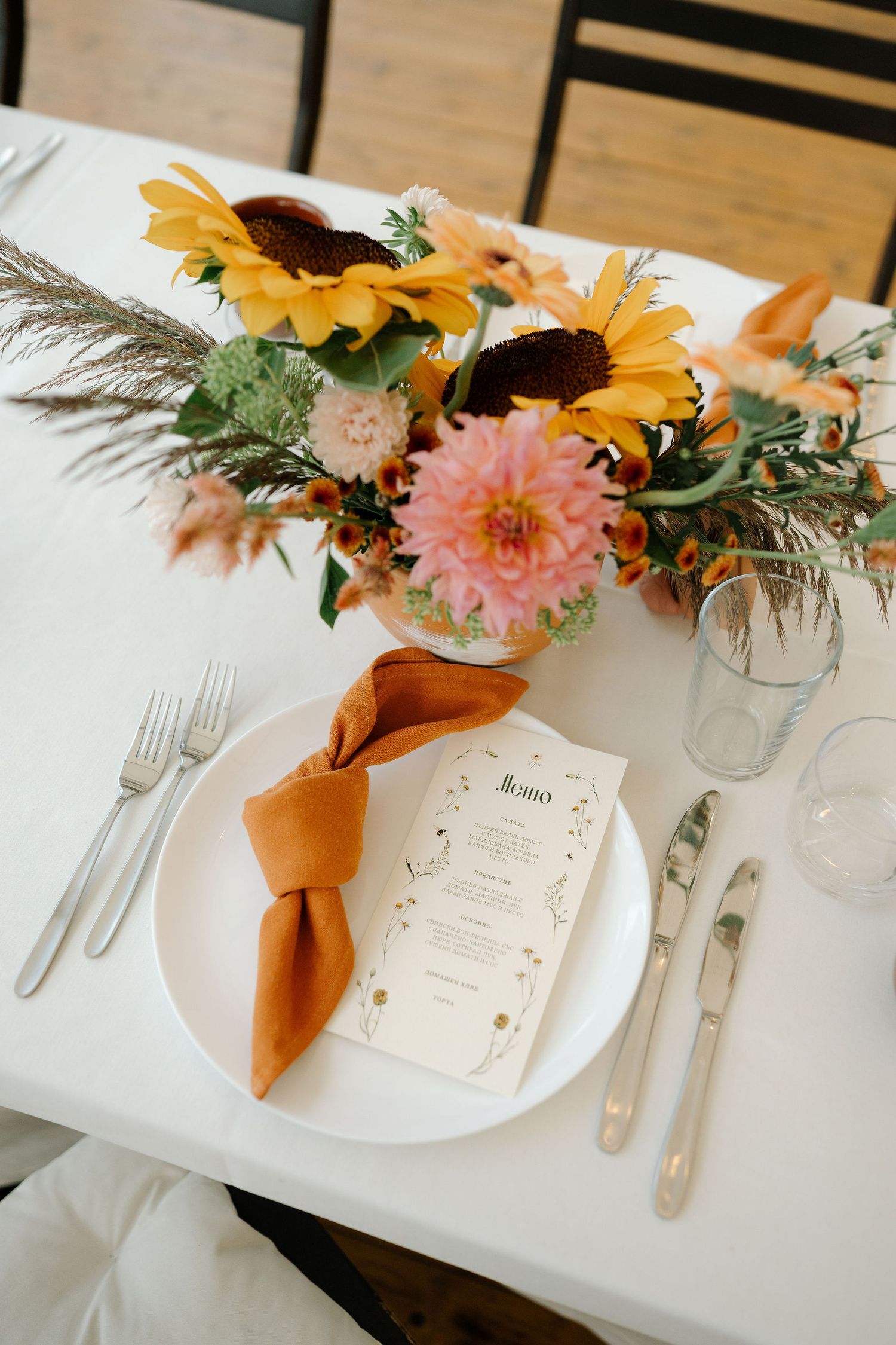 Elegant place settings with autumn-colored flowers and orange napkins arranged on white tablecloths for a wedding reception.