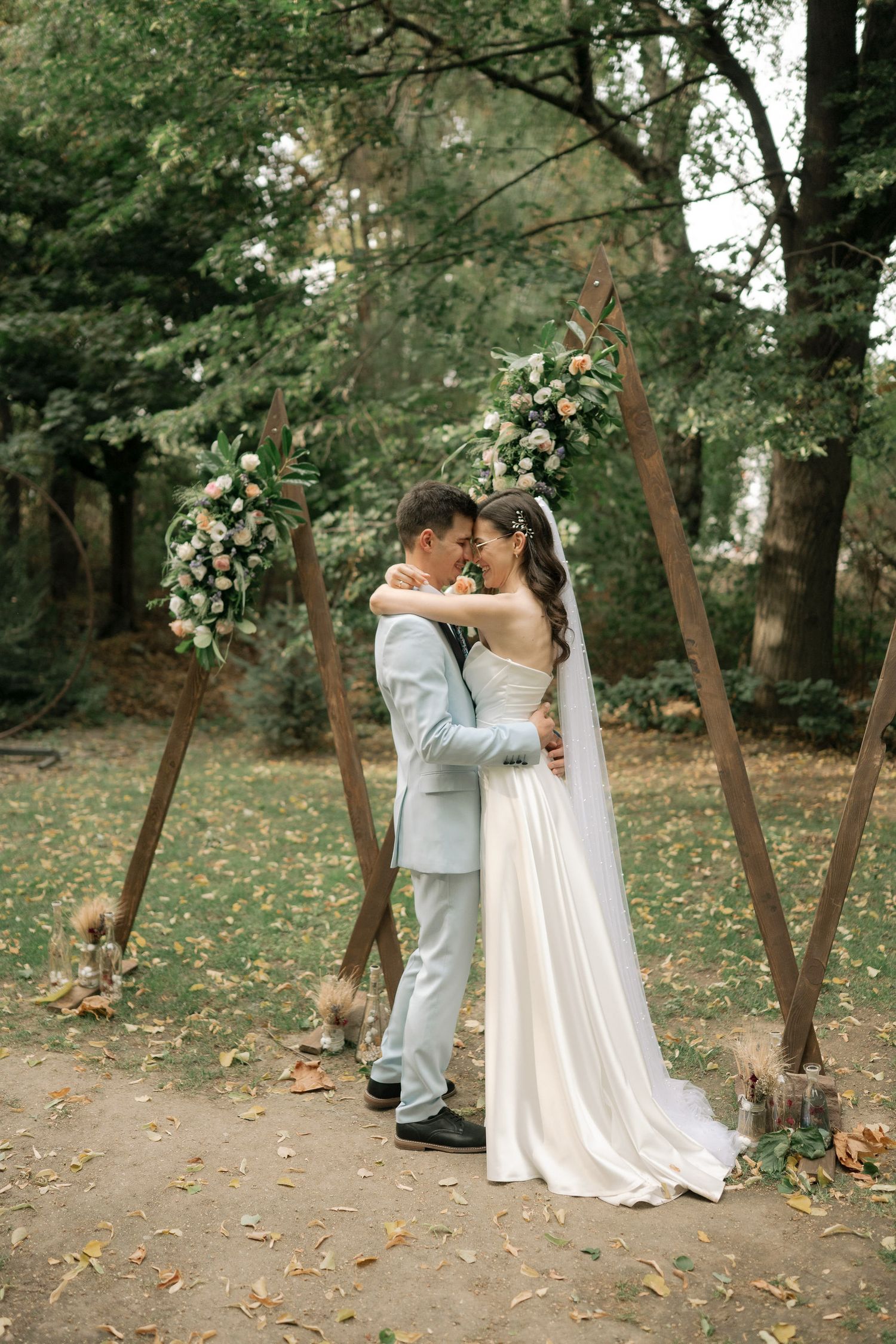 A romantic sequence of wedding photos showing a couple in white and gray attire embracing among autumn trees in a park setting.