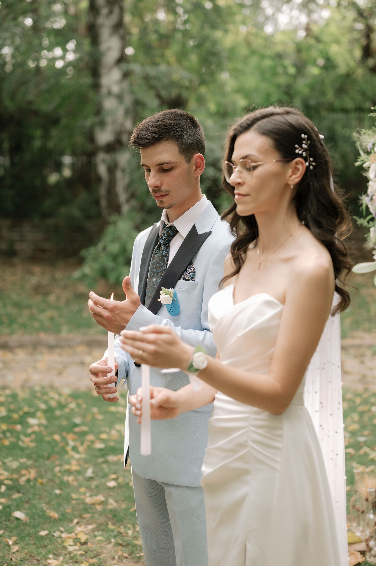 A couple in wedding attire releases white butterflies during an outdoor ceremony in a wooded setting.
