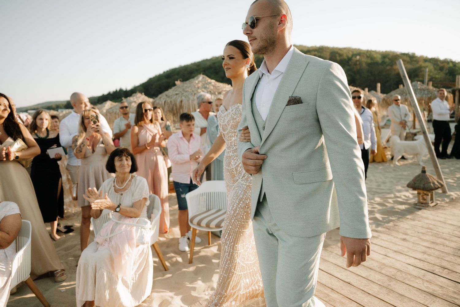 Wedding party celebrates on a beach during sunset with guests dancing and enjoying the festivities.