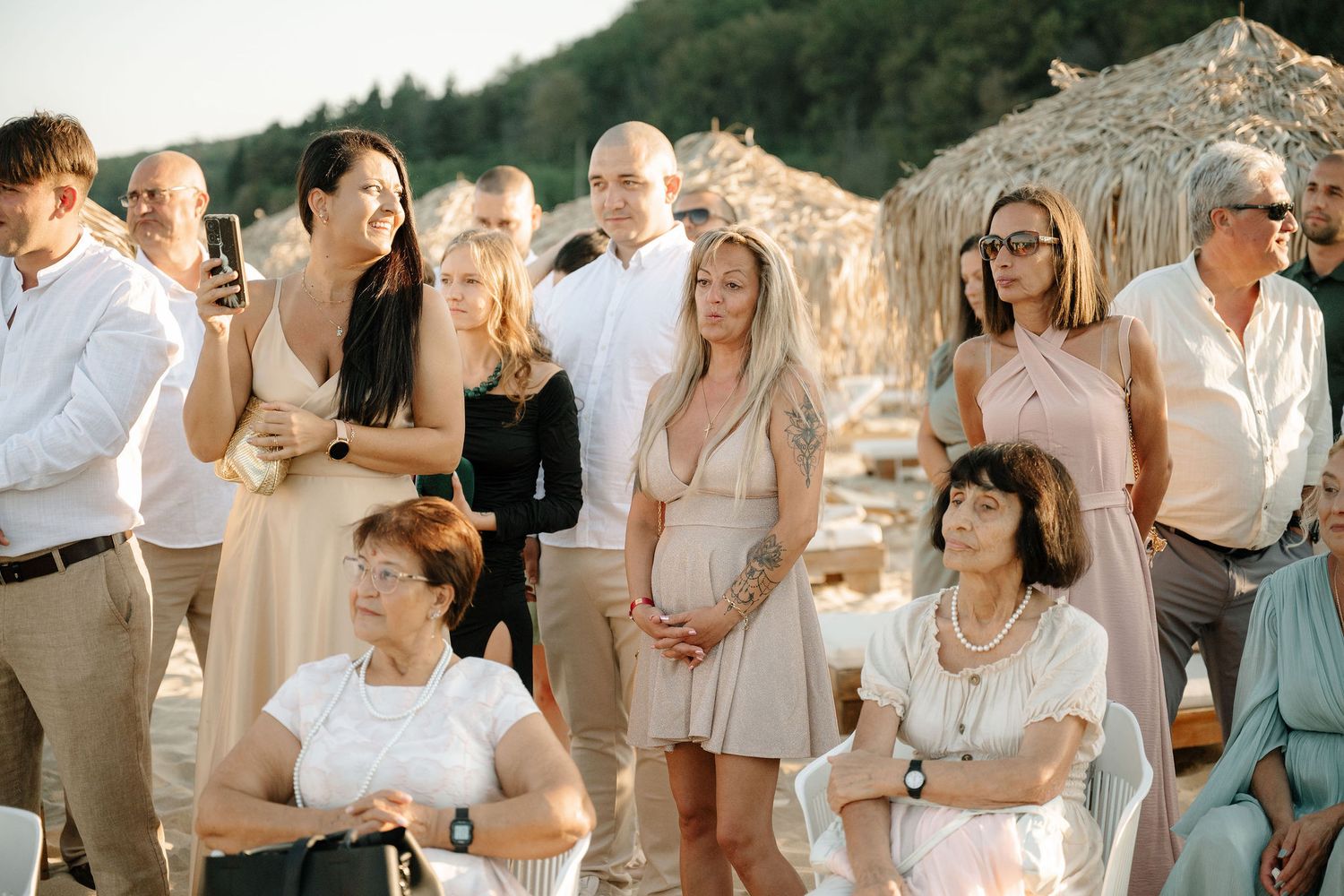 A group of people dressed in light colored outfits gather outdoors for a casual celebration against a rocky backdrop.