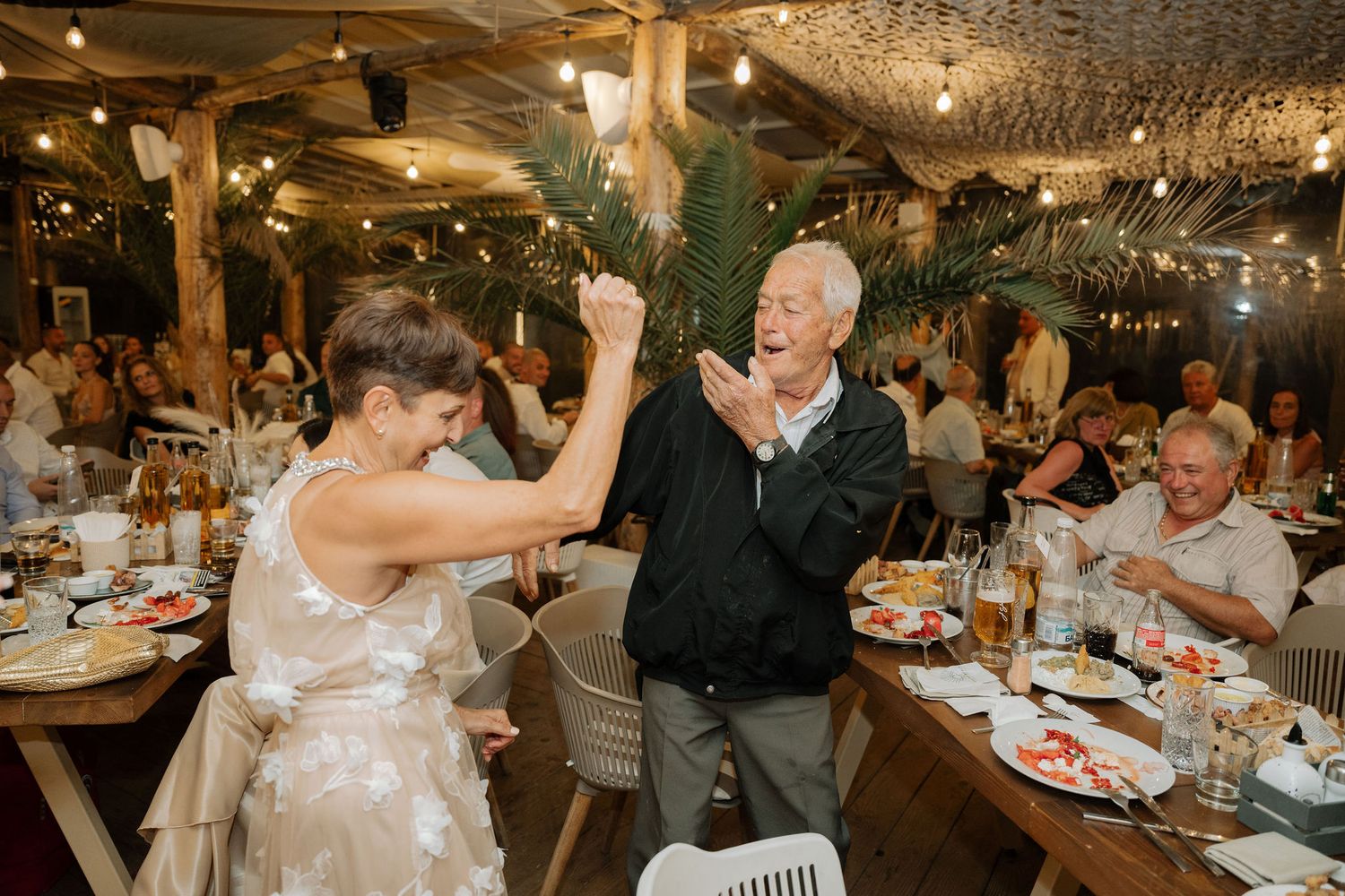 Wedding guests dancing and celebrating at a rustic indoor reception venue with twinkling lights overhead.