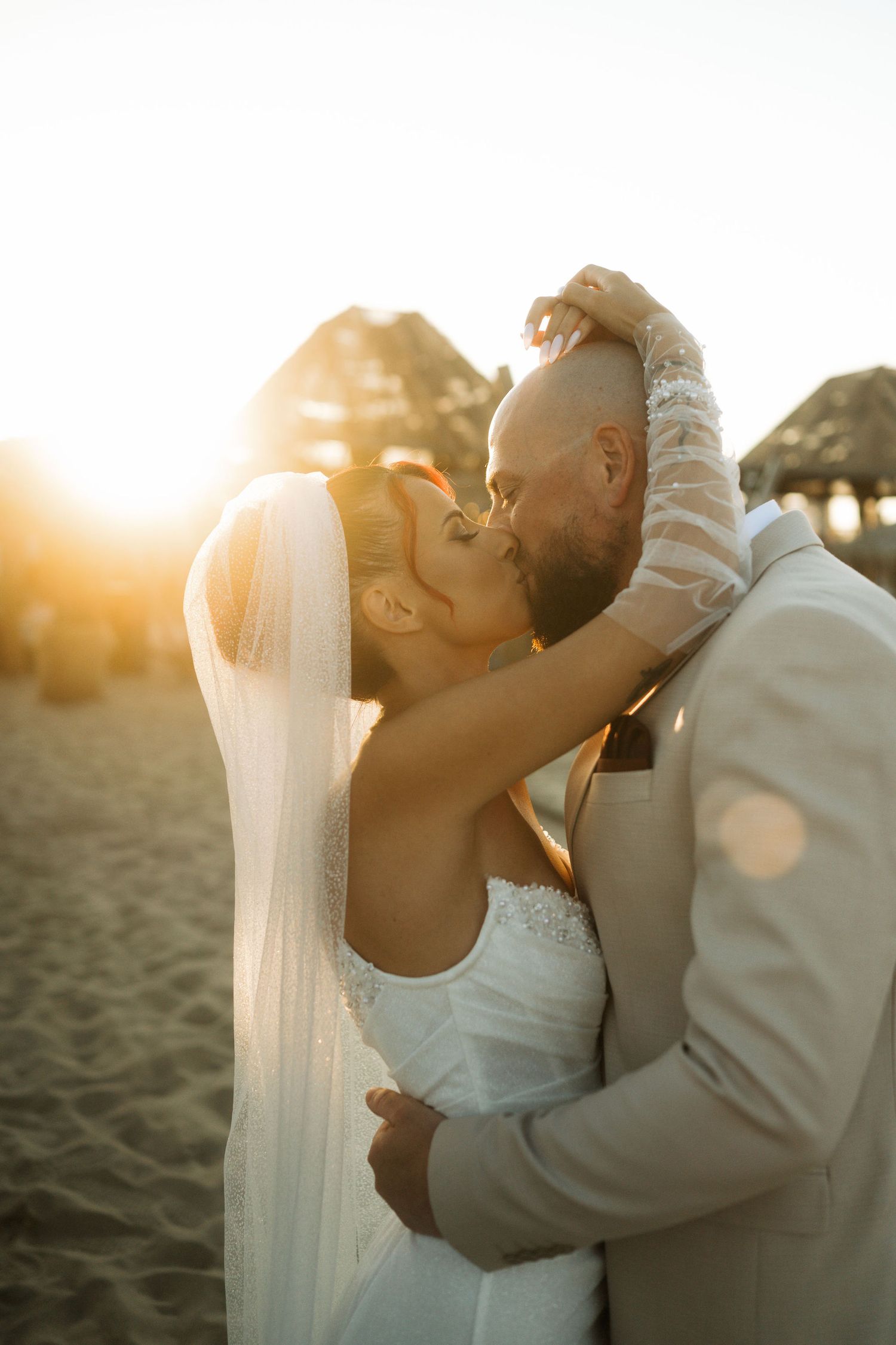 A romantic beach wedding photoshoot with a couple embracing at sunset, creating a warm golden silhouette.
