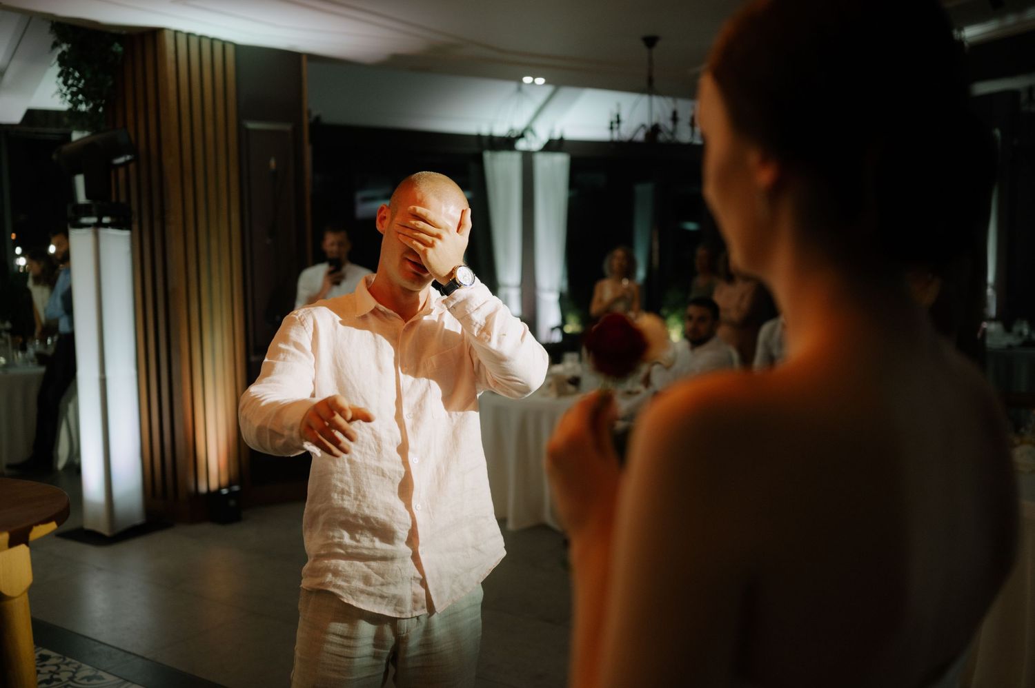 A person in white clothing dances during a wedding reception while guests watch from their tables.