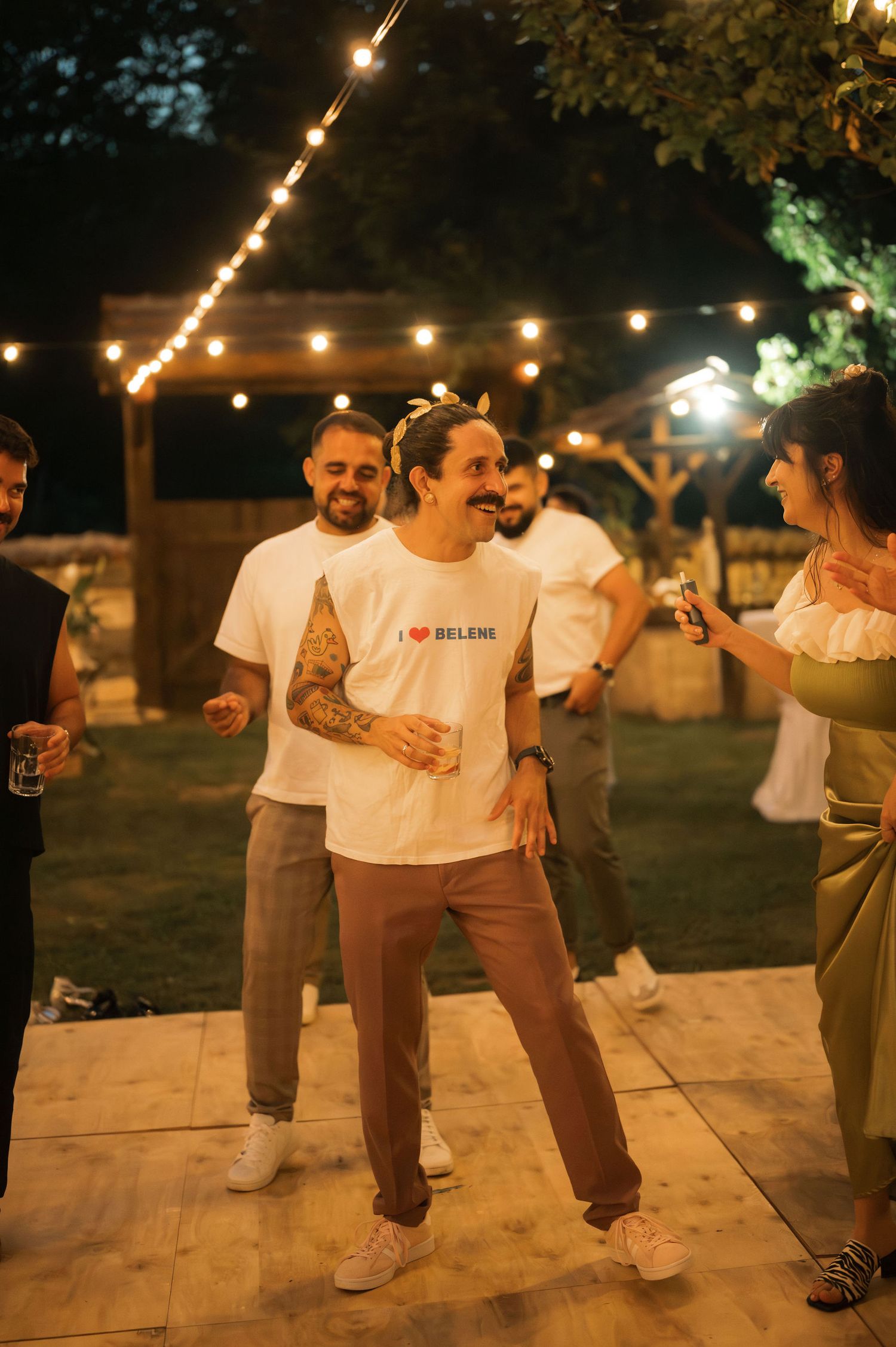 People dancing together outdoors at night under warm string lights on a wooden deck.