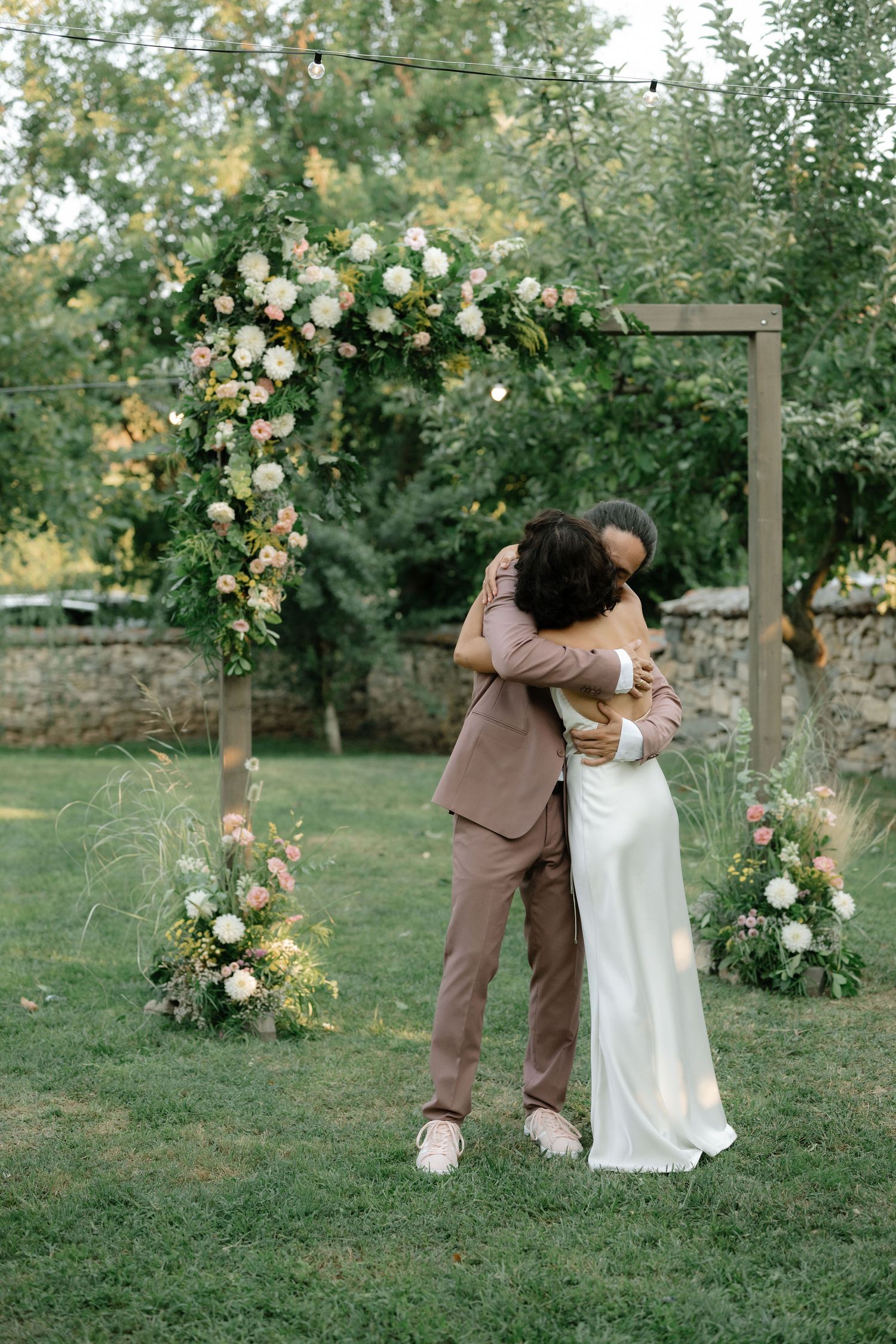 A couple shares a romantic moment in a garden setting with blooming roses and green trees in the background.