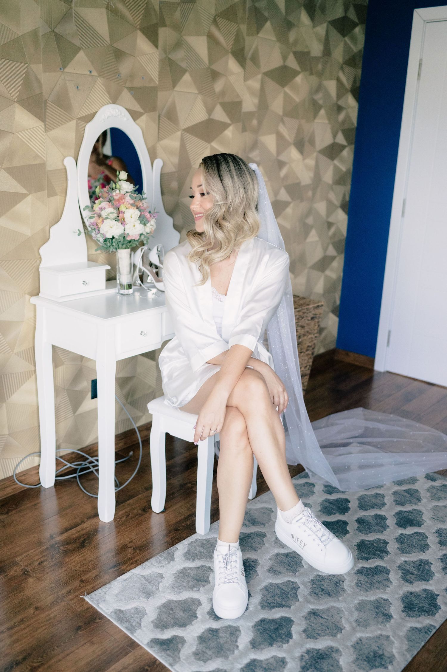 A person in a white outfit sits on a white chair against a geometric wallpapered wall with a blue accent.